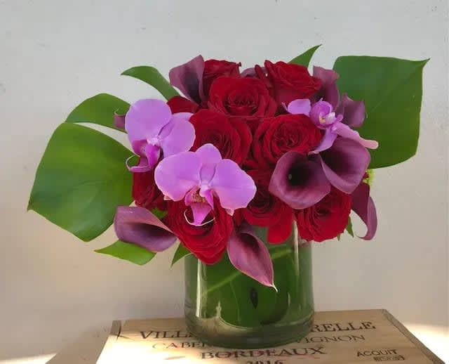 Red roses and purple orchids arranged in a glass vase
