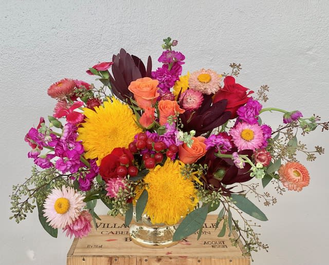 Colorful mixed bouquet in a clear glass vase with yellow, pink, red, and peach blooms.