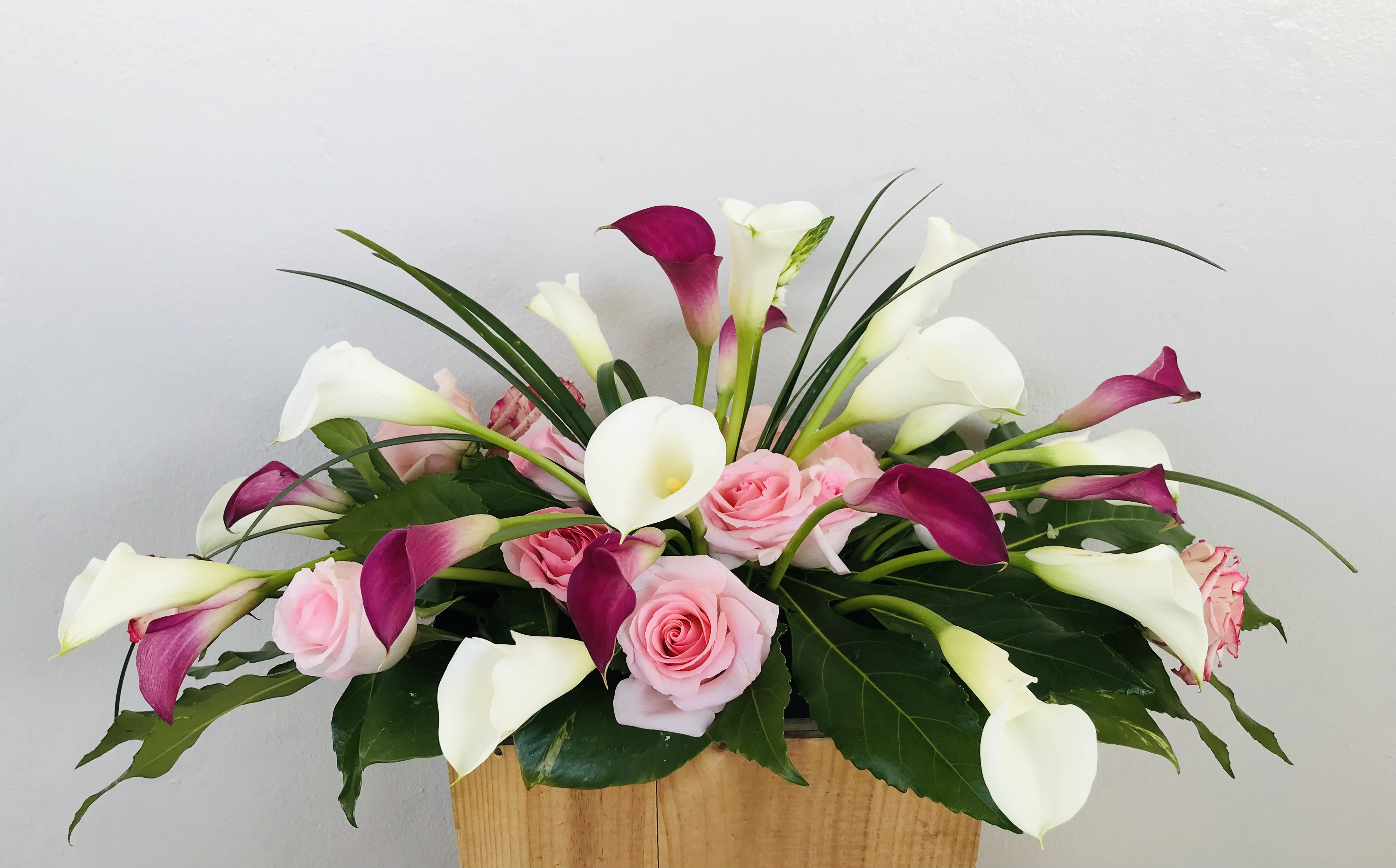 Pink roses and white-purple calla lilies in a wooden container