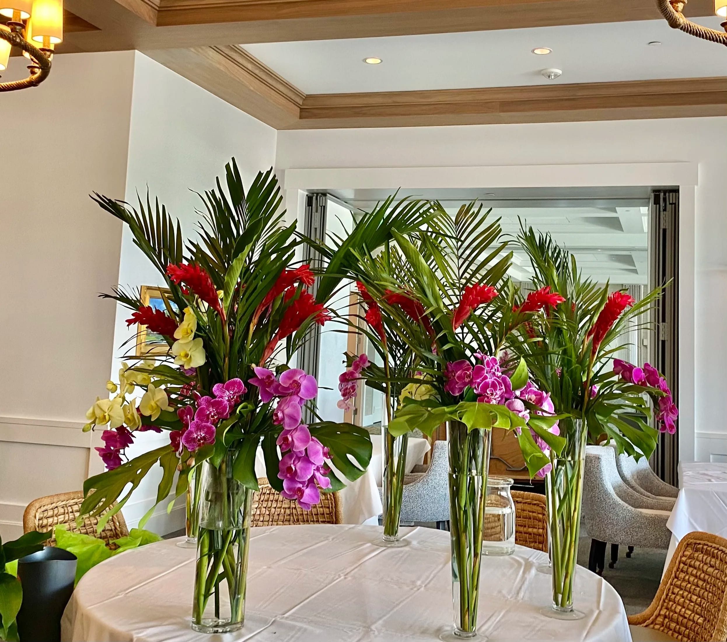 Tall tropical floral centerpieces with orchids and red blooms in glass vases