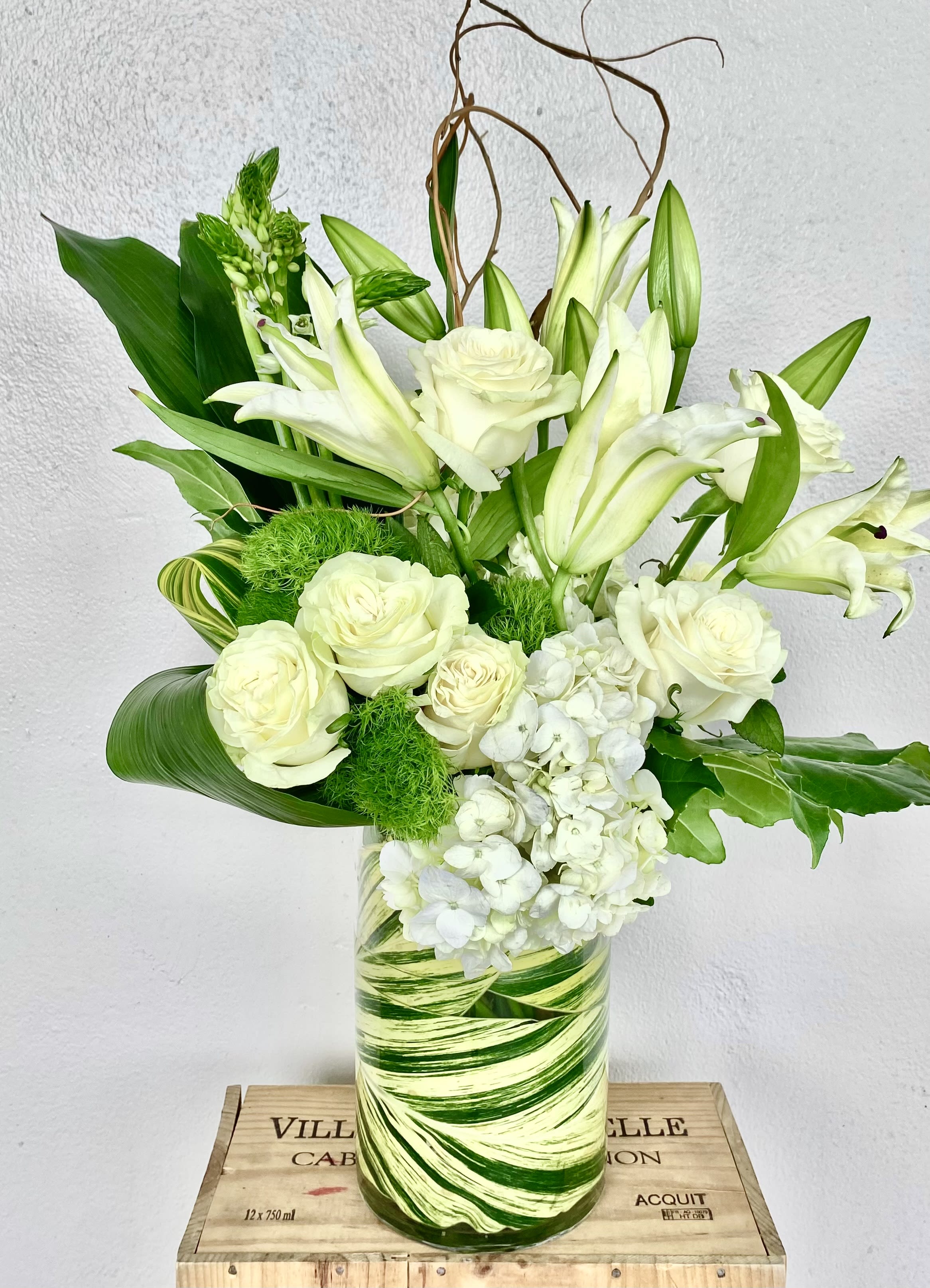 White roses and lilies arranged in a green-striped glass vase