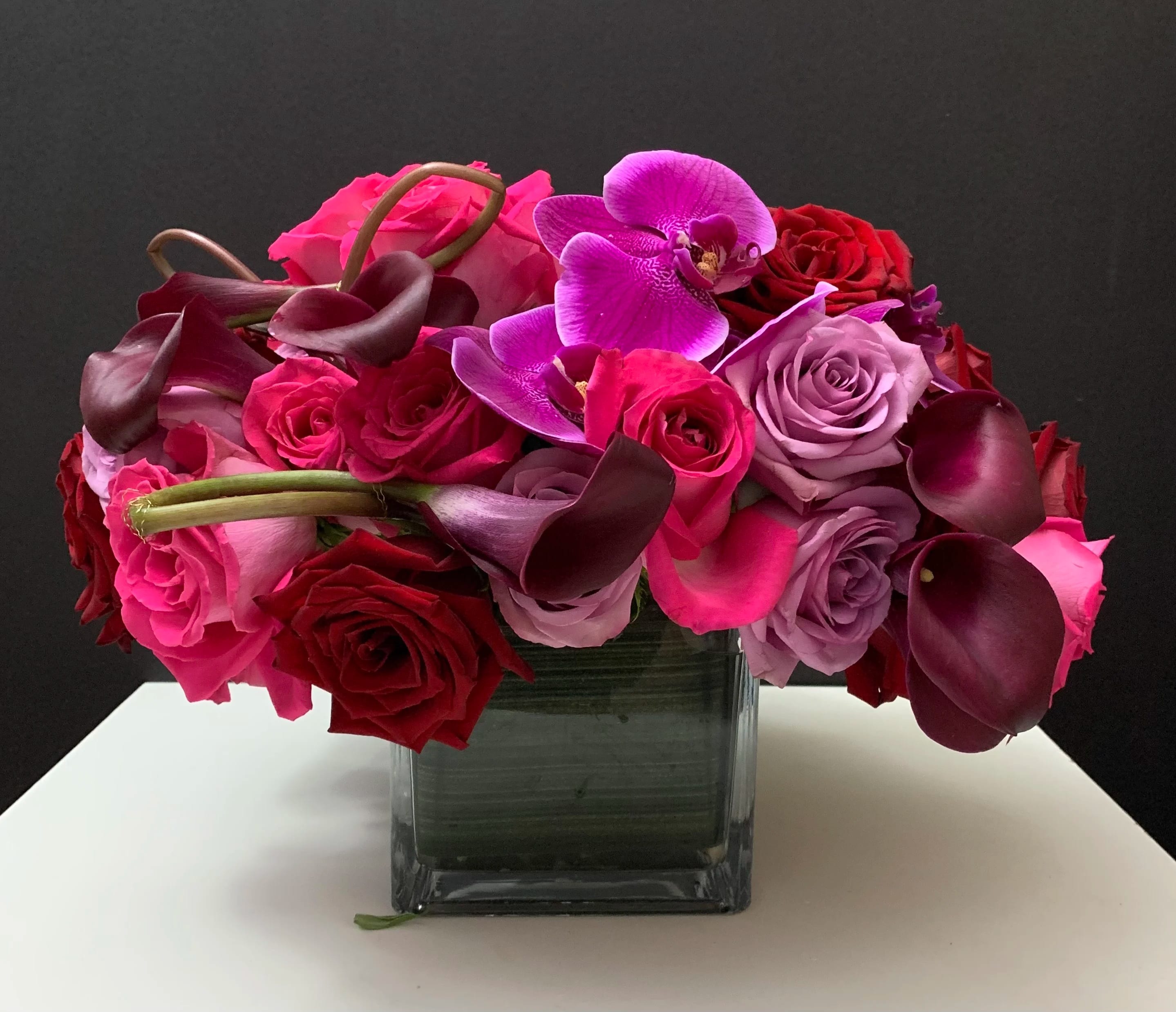Bouquet of pink and red roses with purple orchids in a square glass vase
