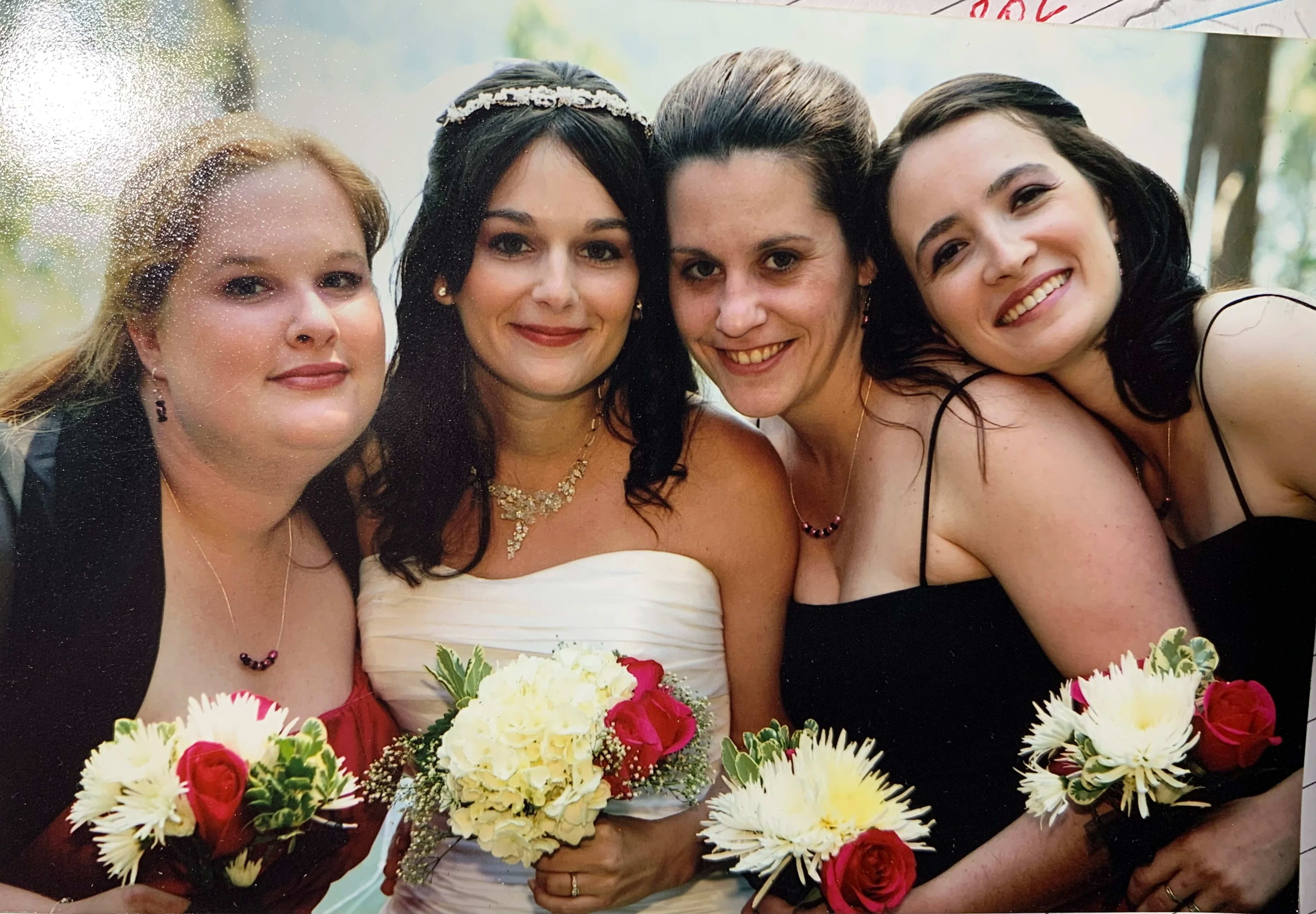 Four women in formal dresses holding small bouquets of white and red flowers