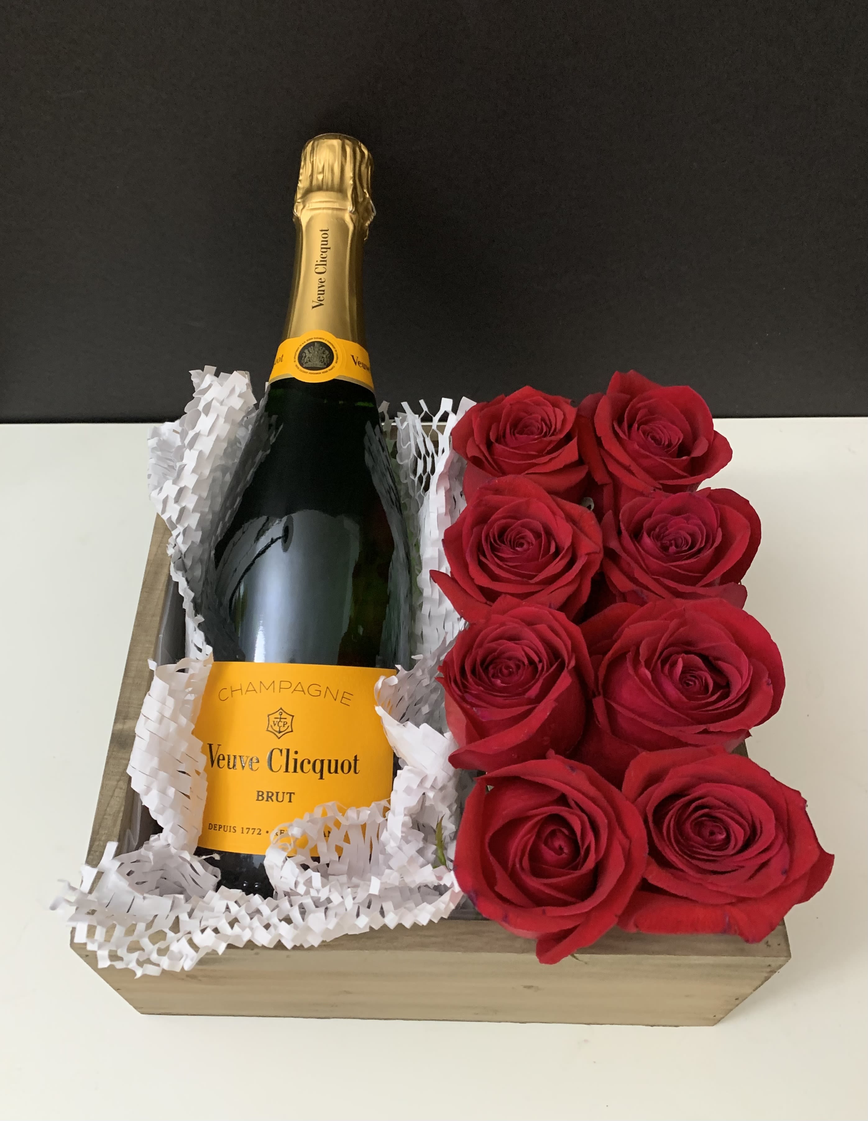 Champagne bottle in a wooden gift box beside red roses