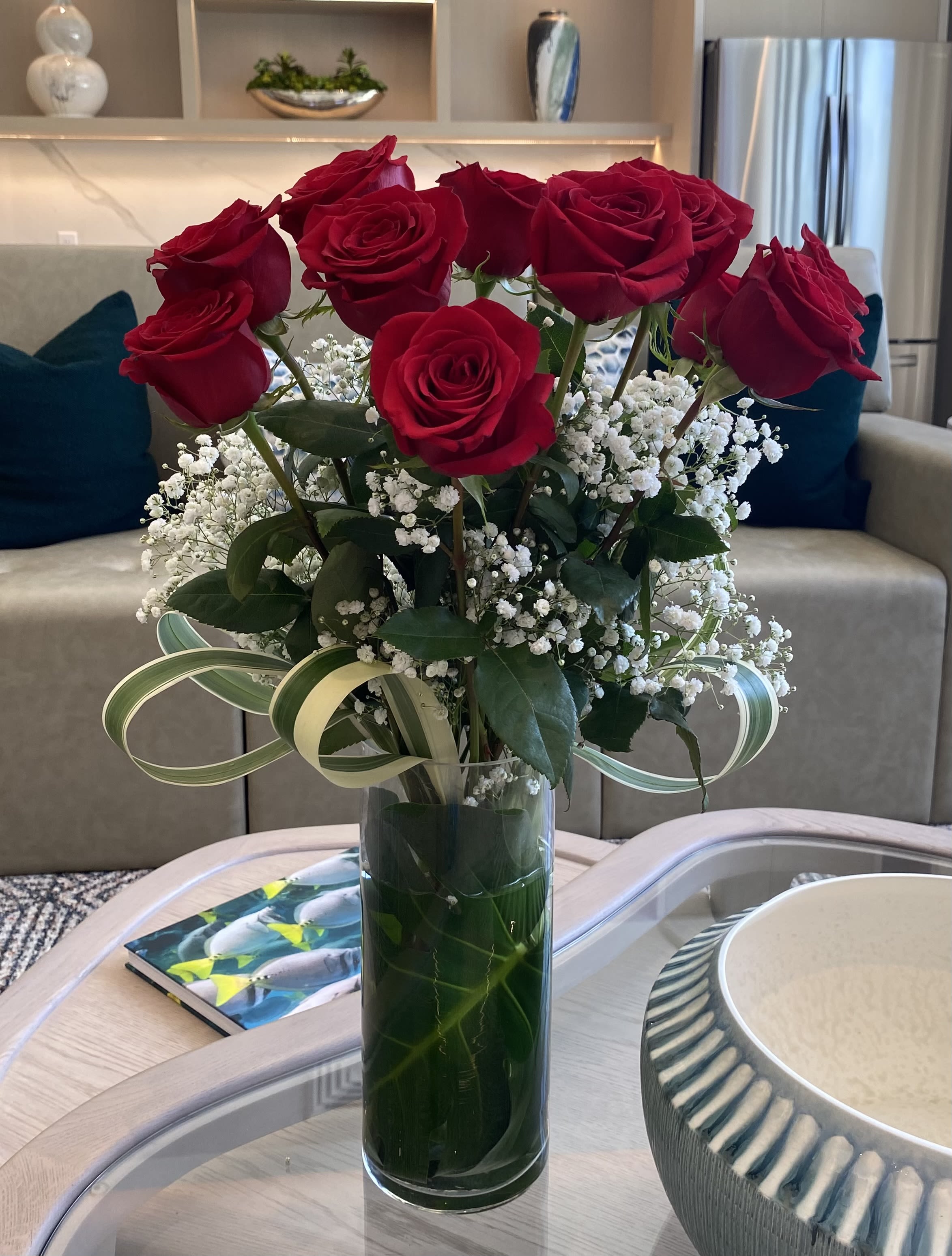 Red roses arranged in a tall glass vase with white baby's breath