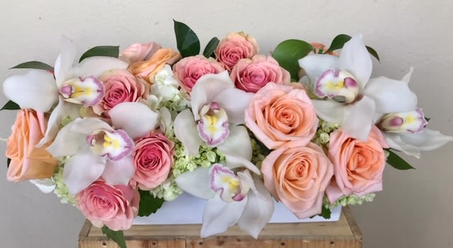 Pink and peach roses with white orchids in a white rectangular box