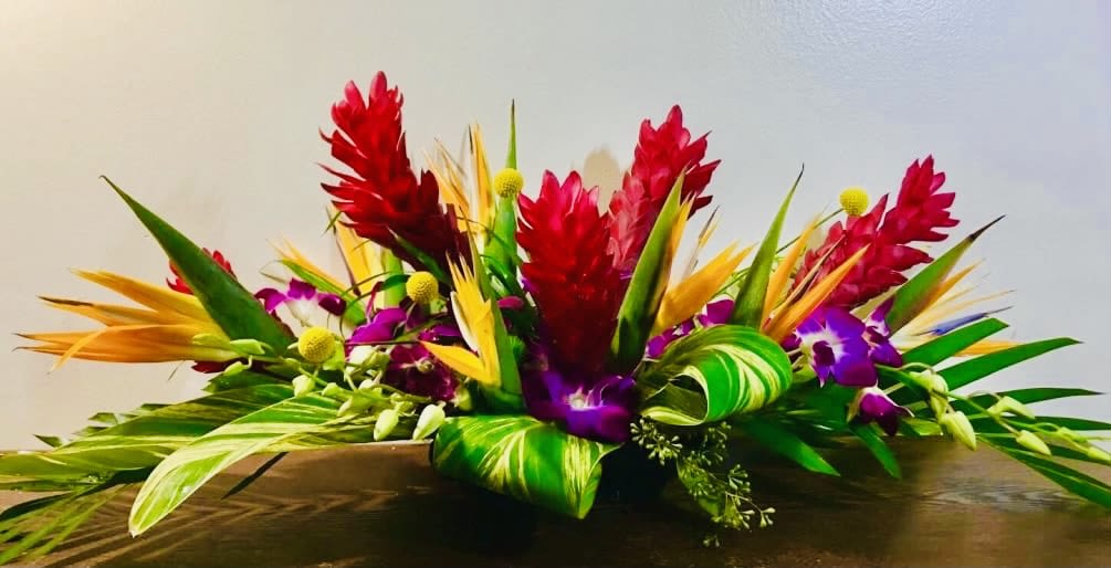Tropical flower arrangement with red, purple, and yellow blooms in a low container