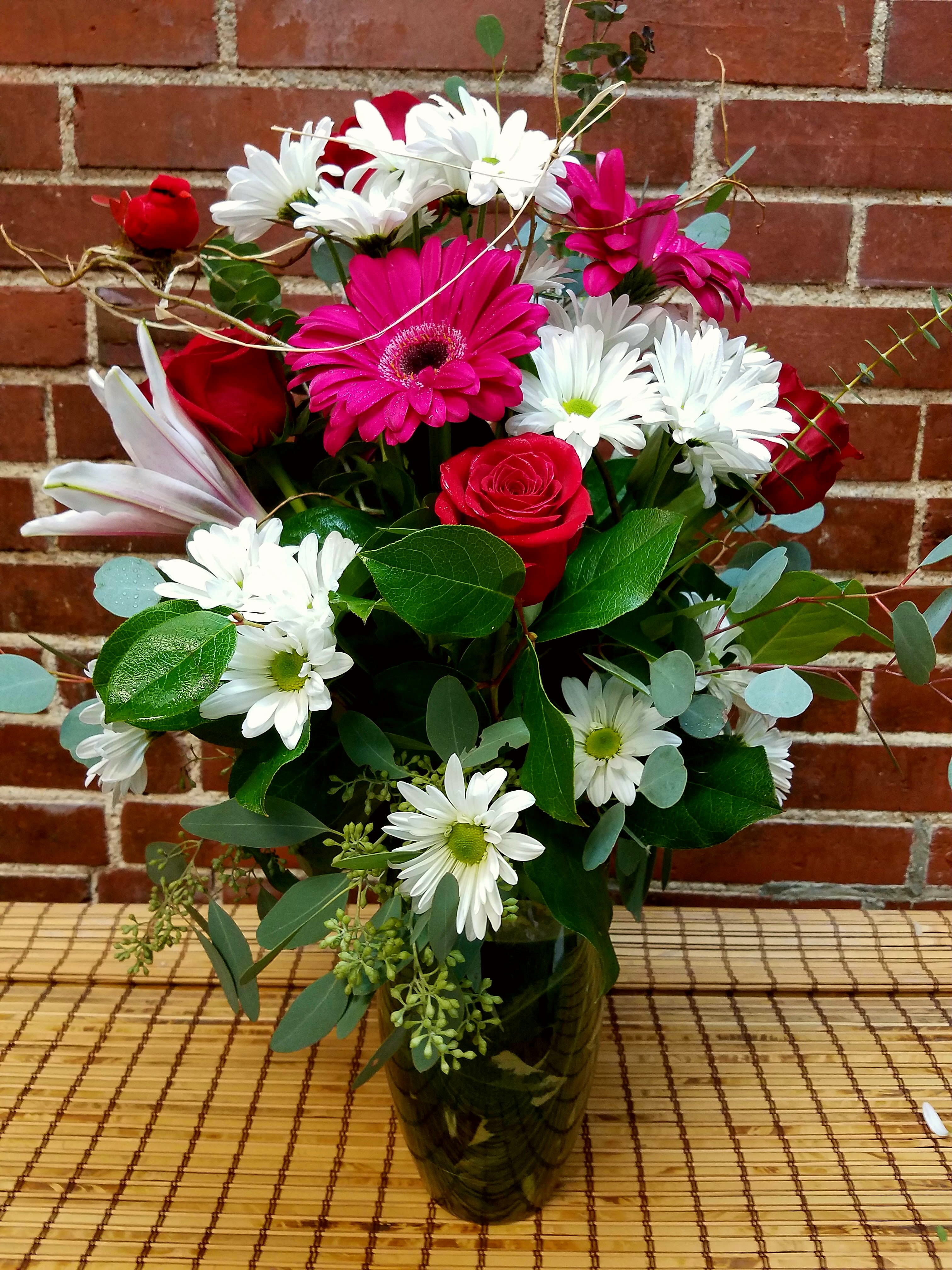 Bouquet of red roses, pink gerberas, and white daisies in a glass vase