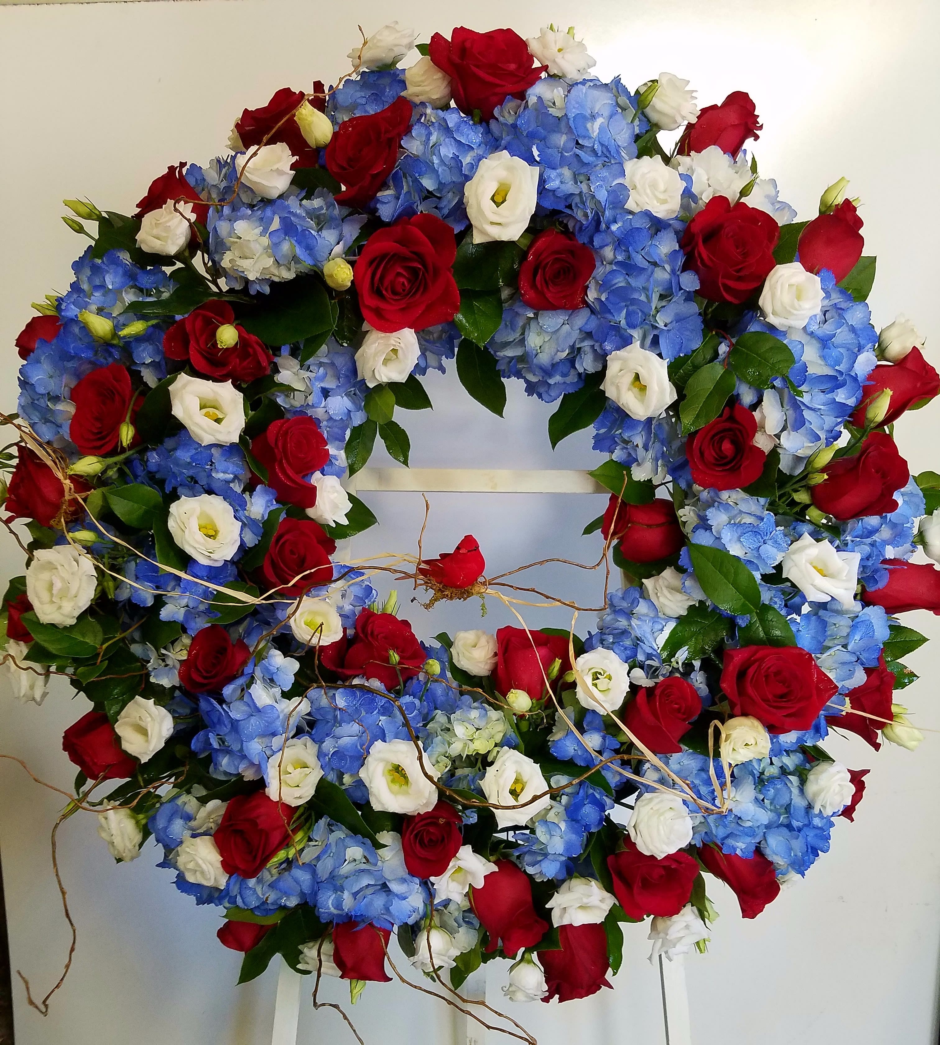 Circular wreath of red roses, blue hydrangeas, and white blooms