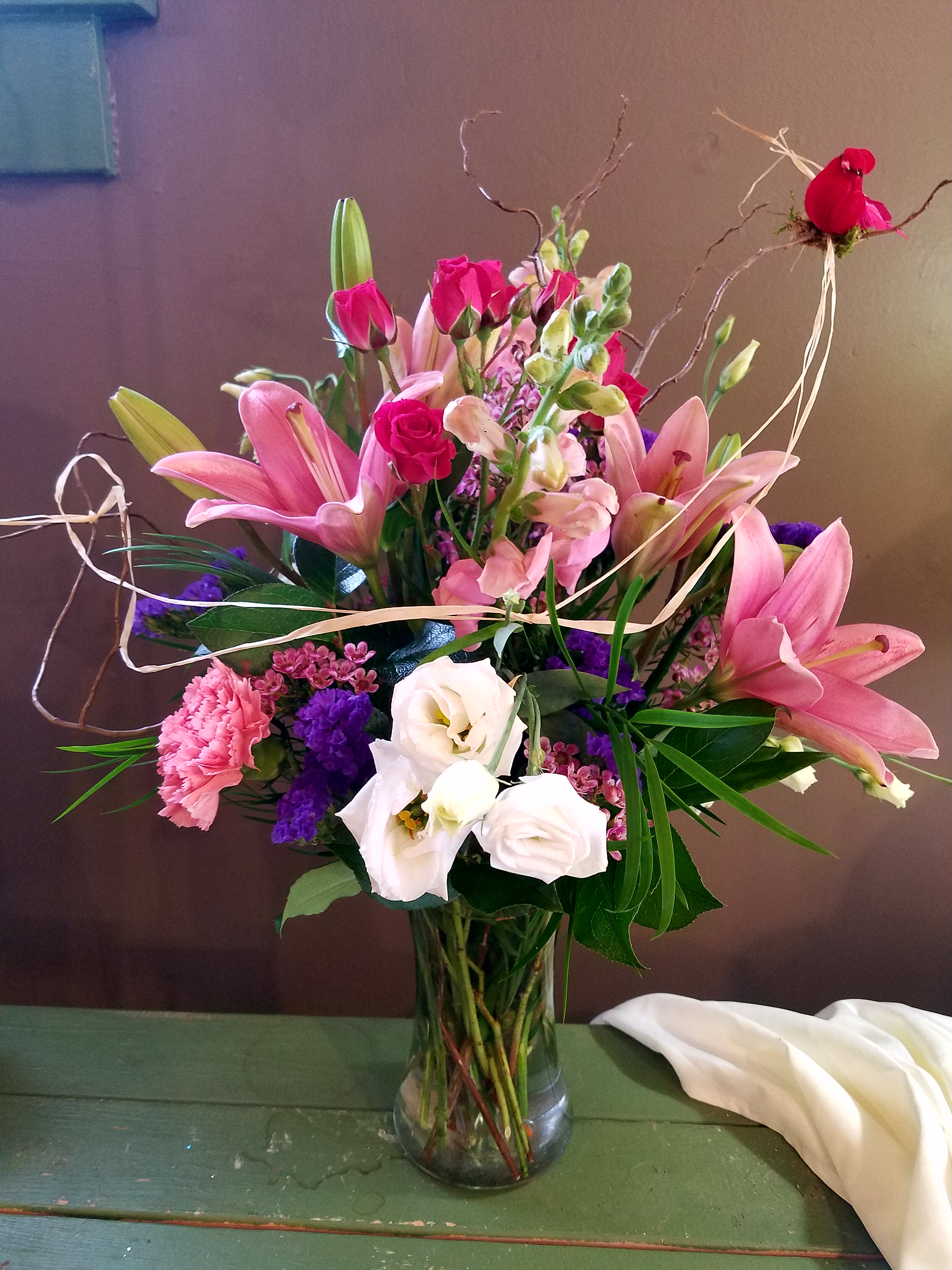 Pink lilies, roses, and white blooms arranged in a glass vase