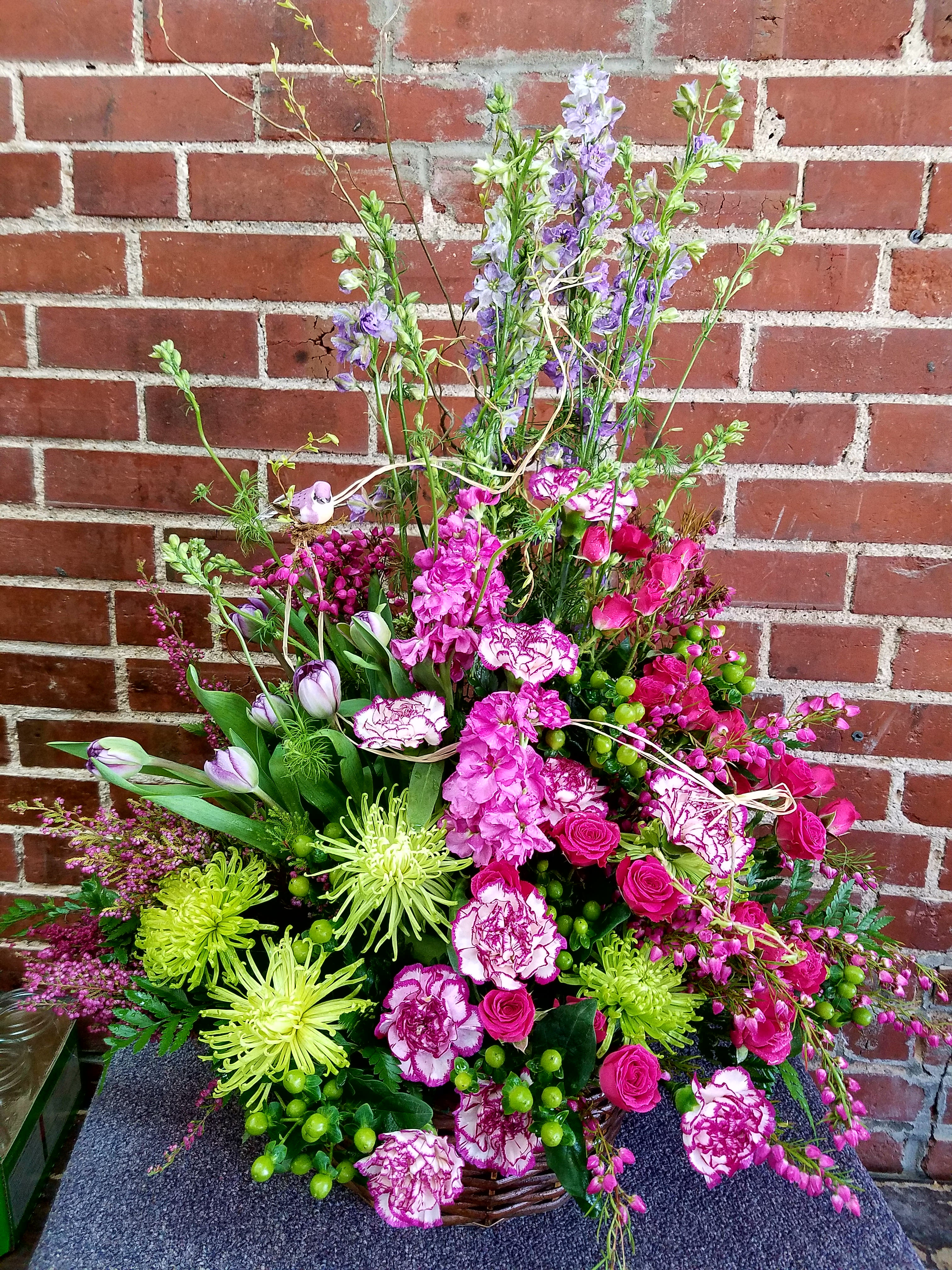 Tall basket arrangement with pink blooms, green spider mums, purple delphinium, and tulips