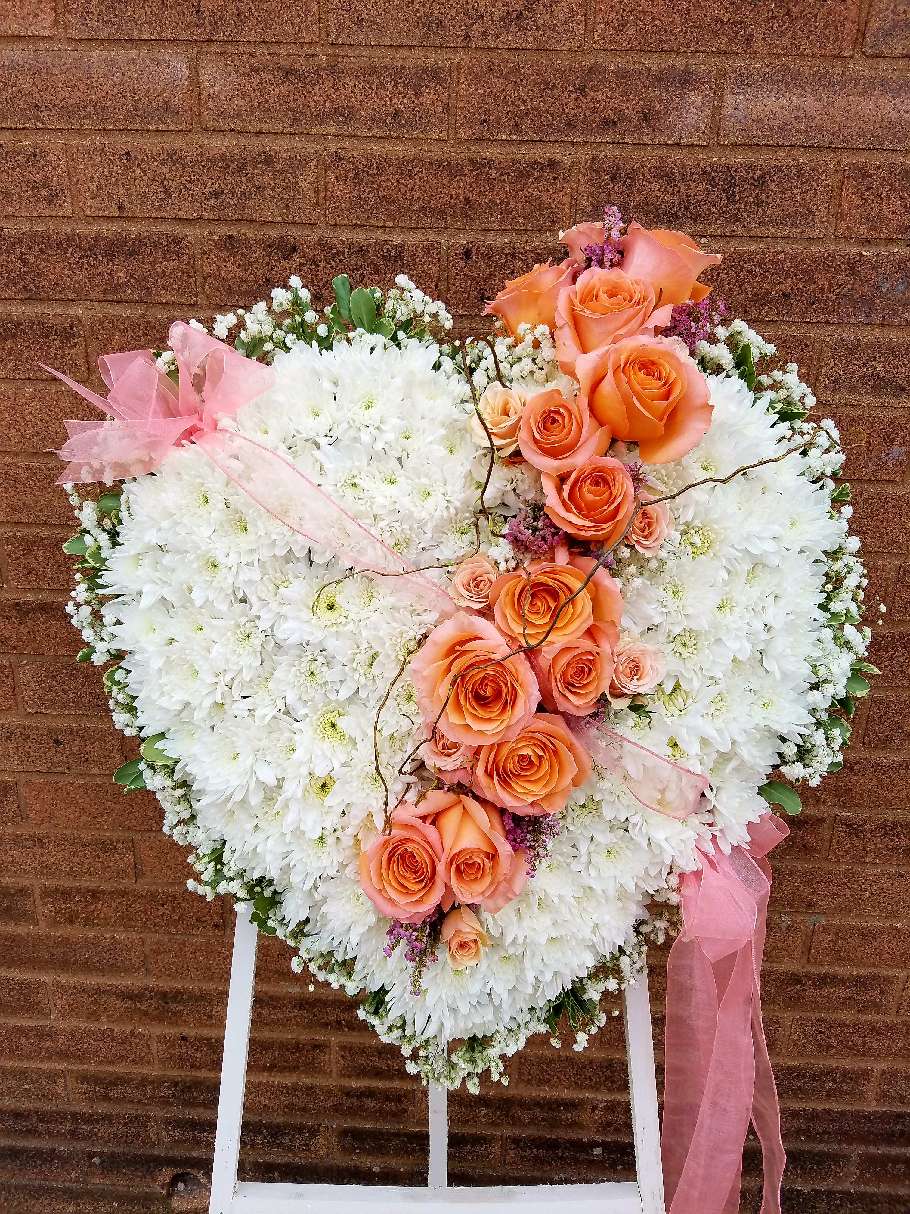 Heart-shaped floral spray with white chrysanthemums and peach roses on a stand