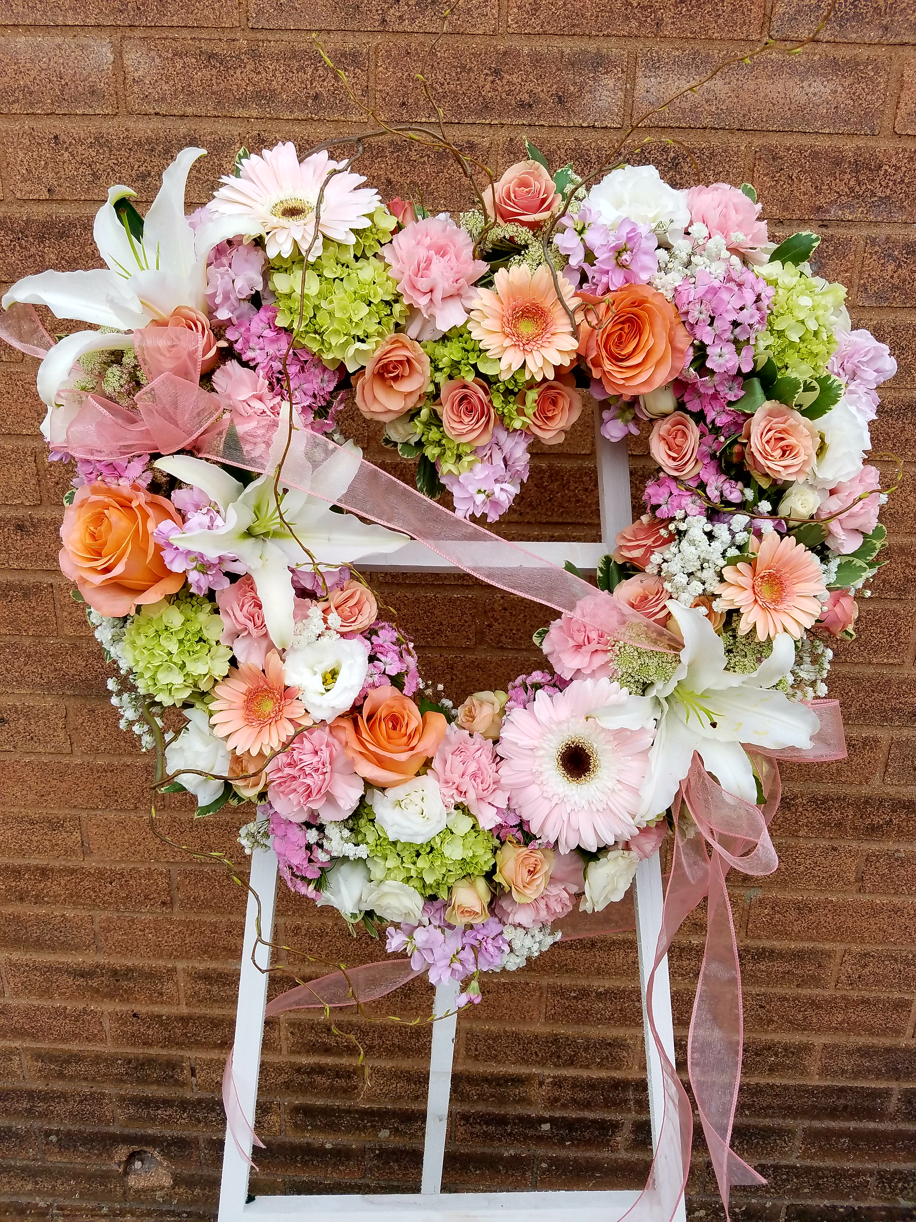 Heart-shaped floral wreath with pink, peach, and white flowers on a stand