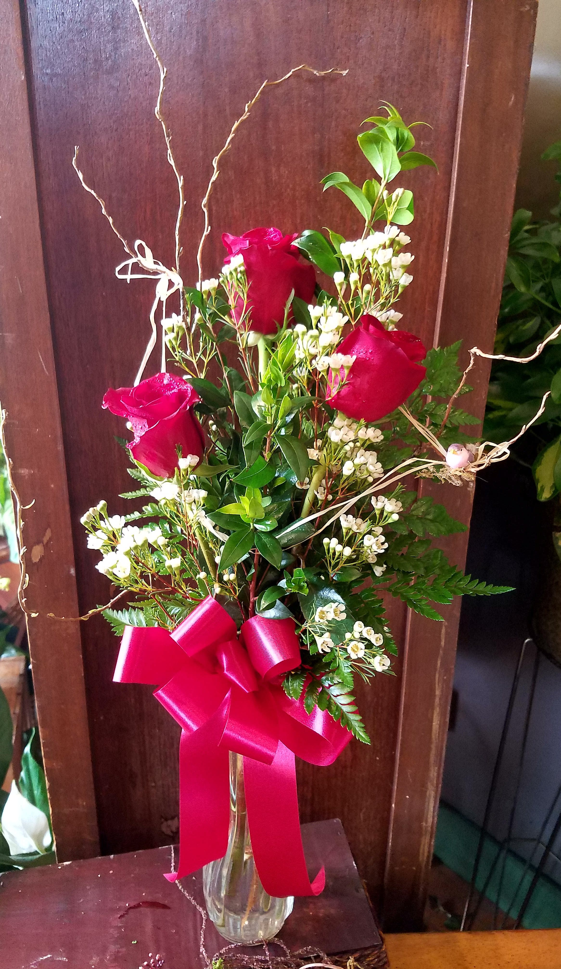 Red roses in a clear glass vase with a pink ribbon bow