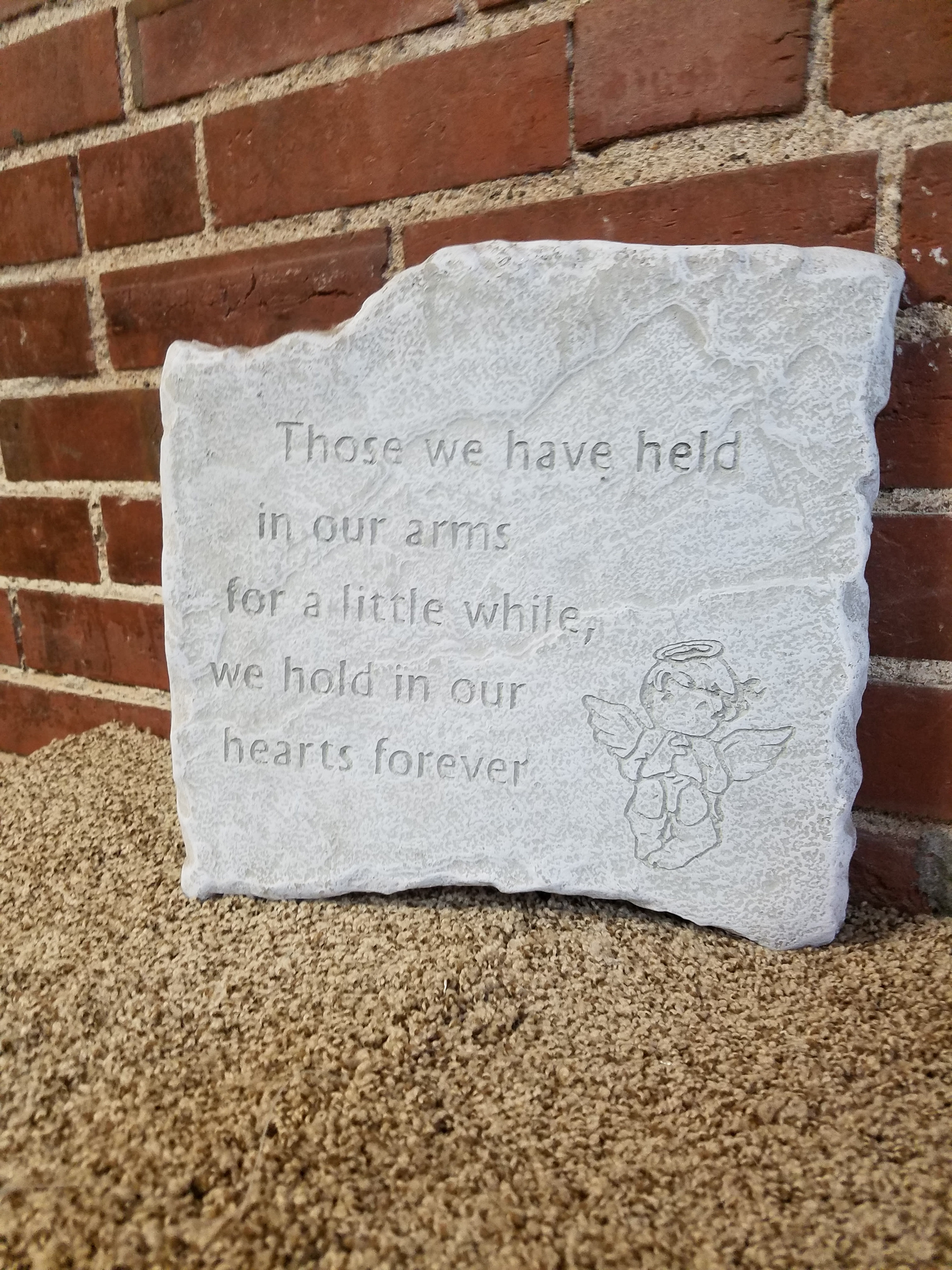 A white memorial stone plaque with an angel engraving and engraved text.