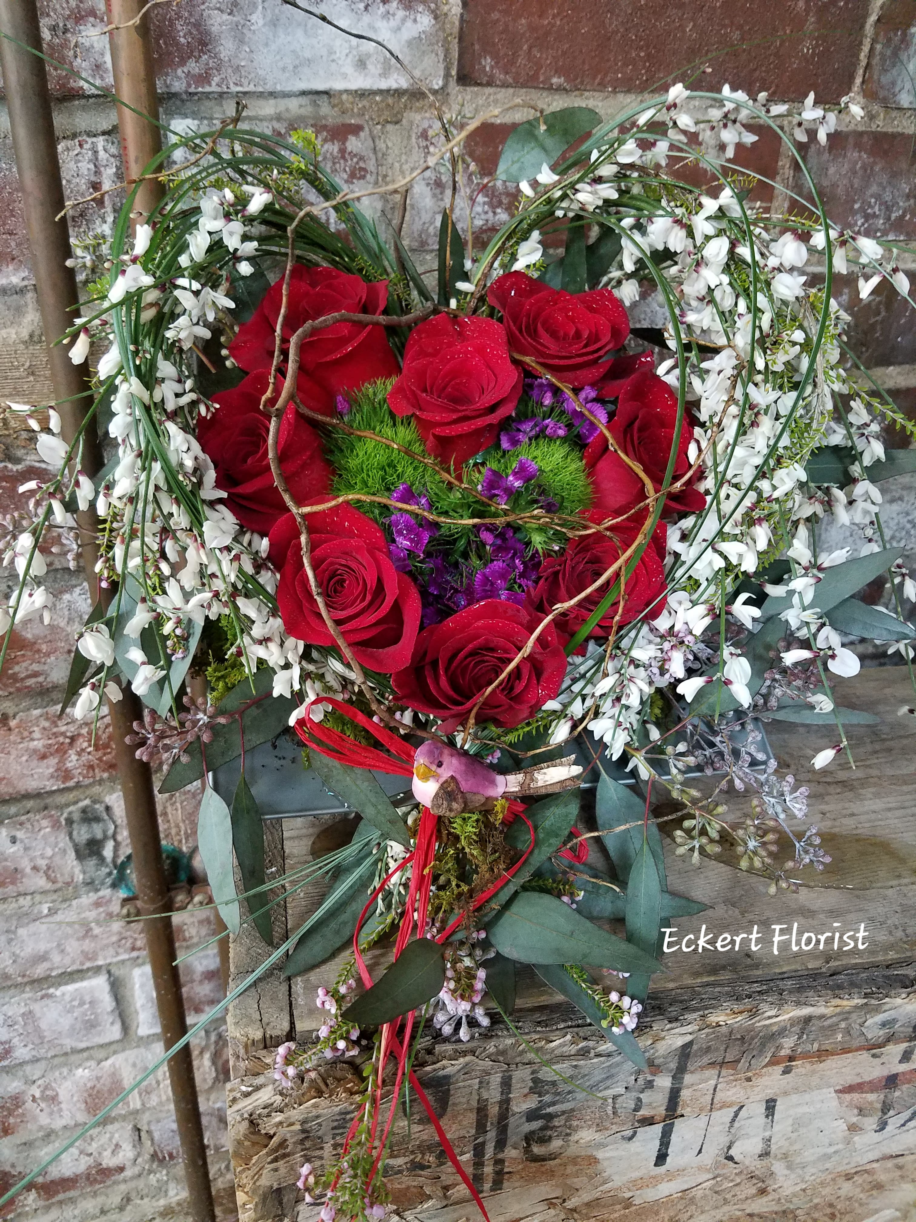 Heart-shaped bouquet of red roses with white blossoms and purple accents