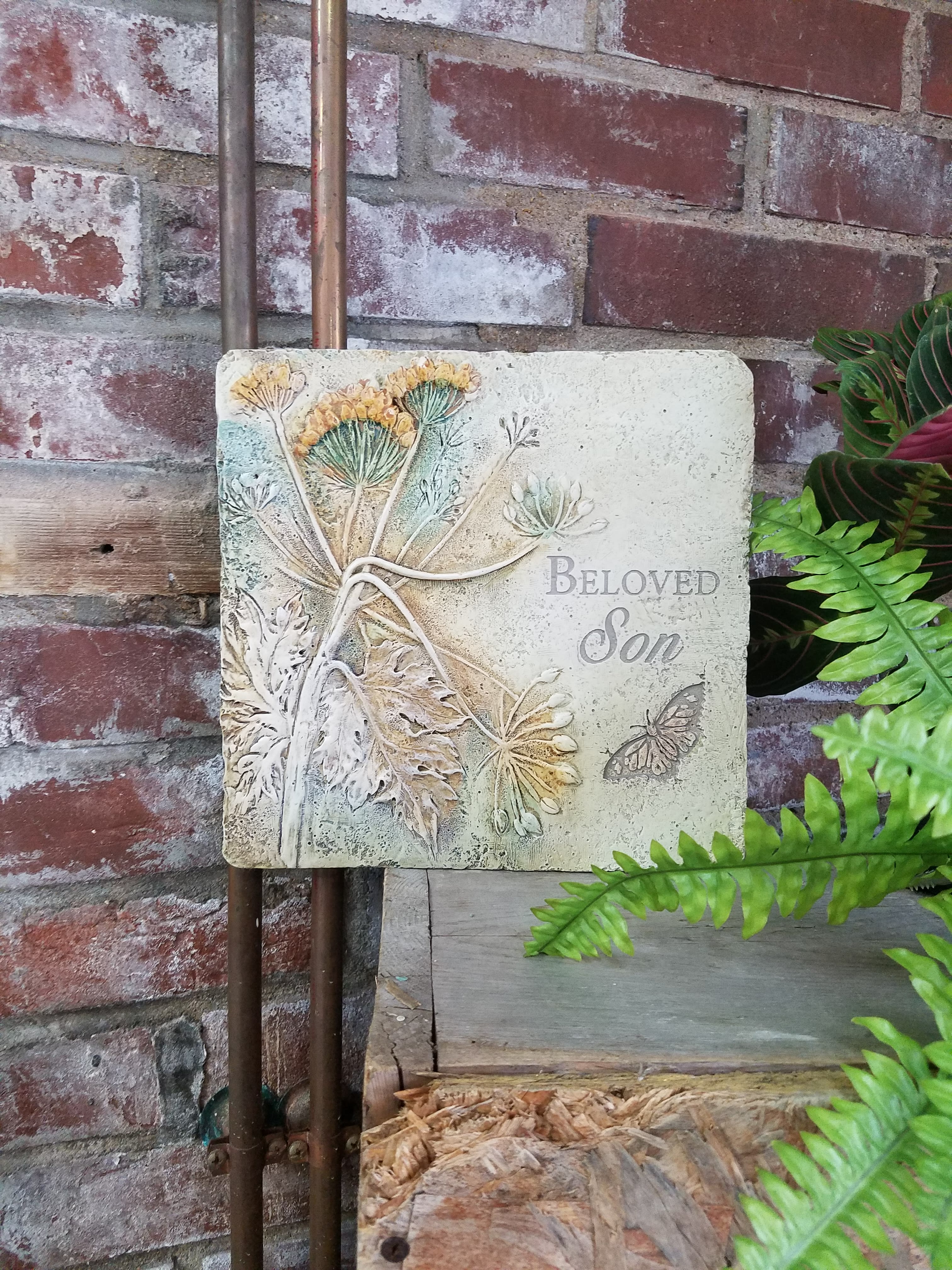 Decorative memorial plaque reading "Beloved Son" with floral relief and butterfly