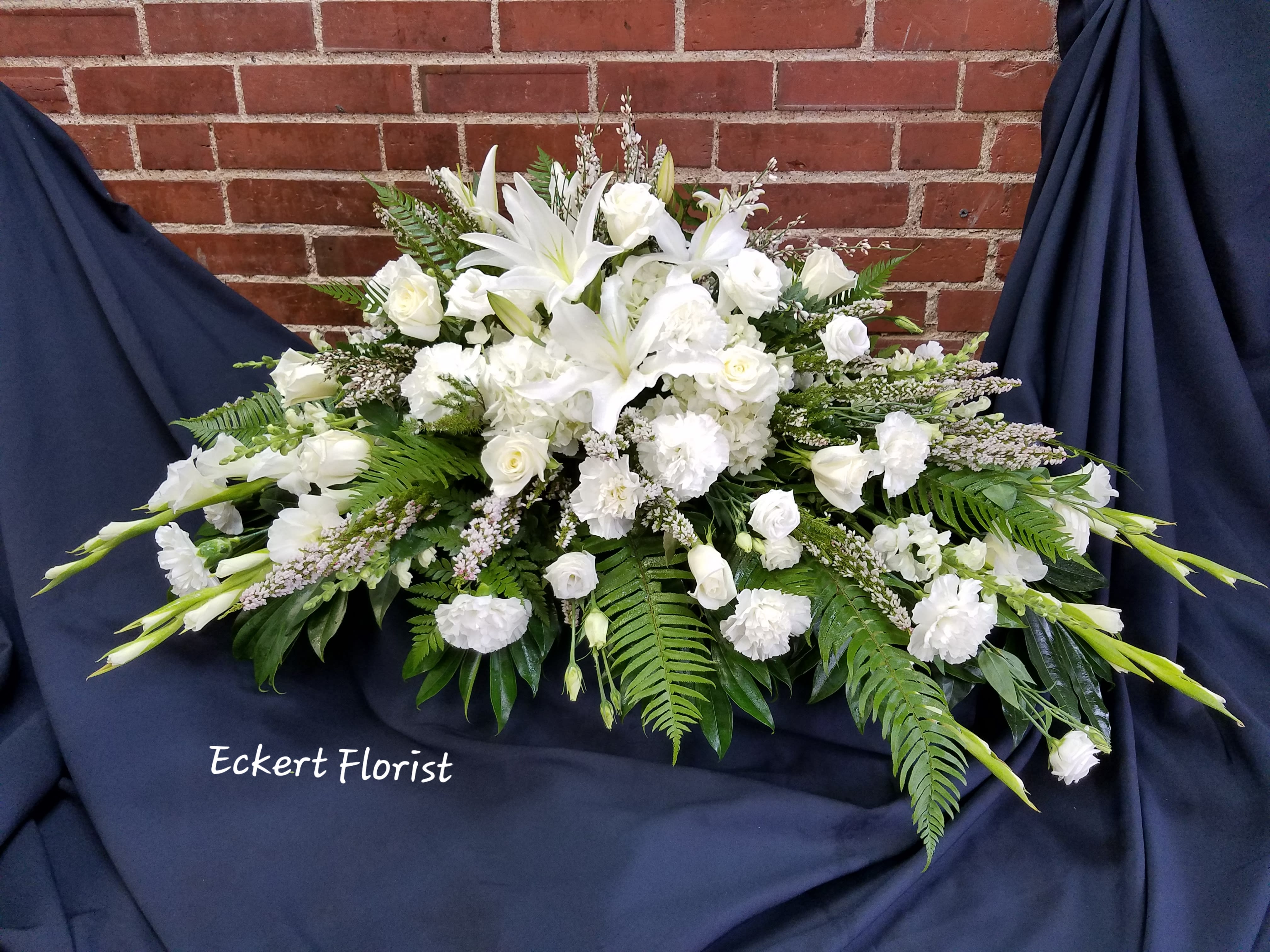 White funeral spray with lilies and roses on dark drape