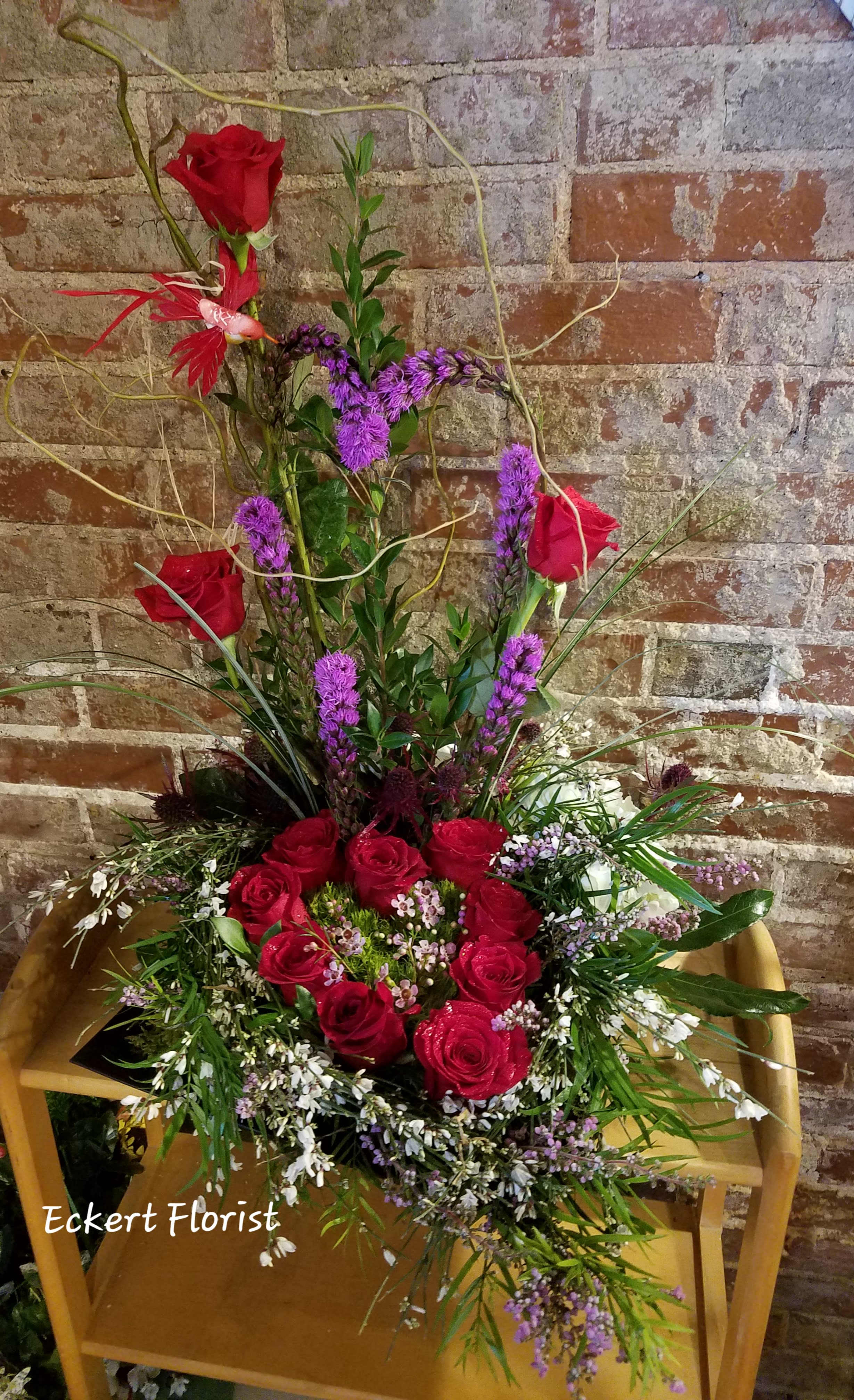 Tall arrangement of red roses and purple flowers in a wooden chair