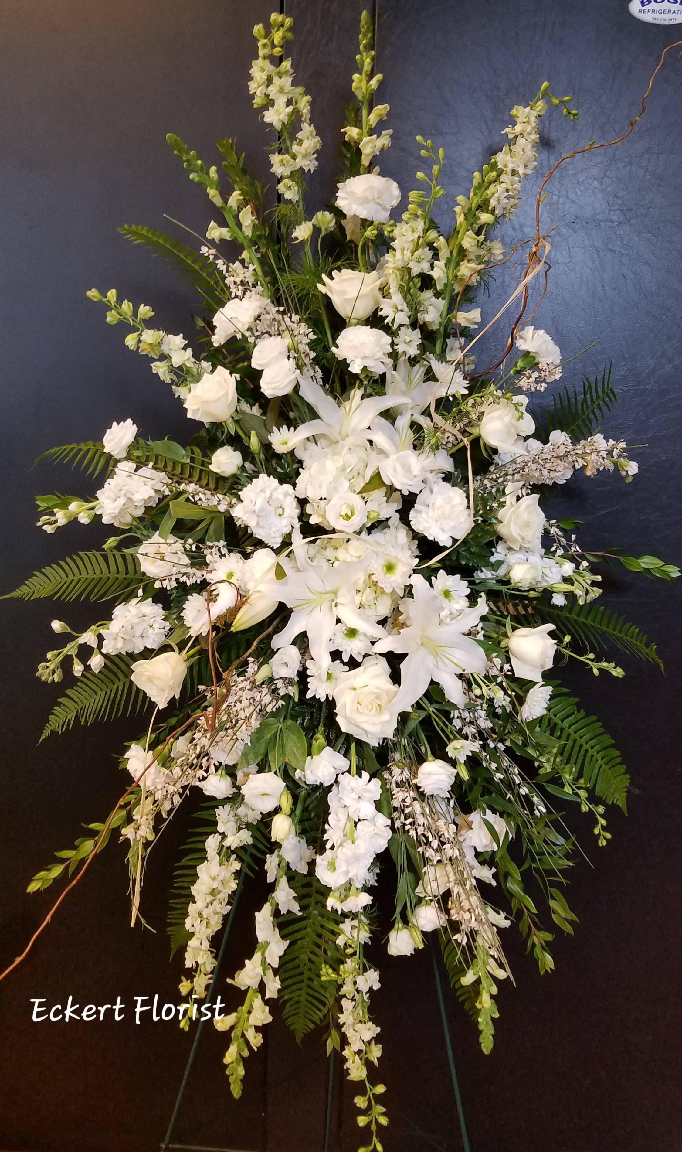 Tall white funeral spray with lilies, roses, and snapdragons