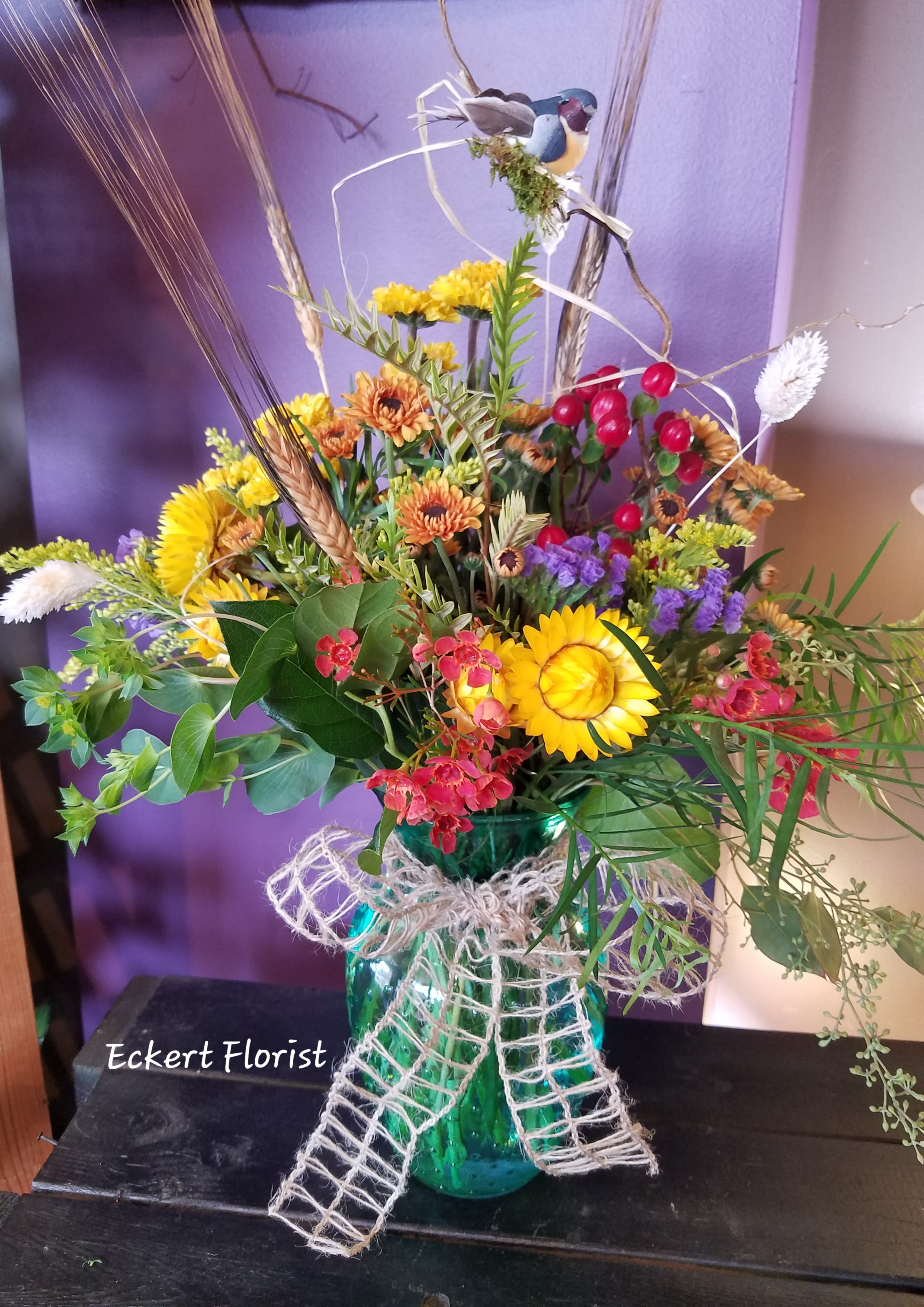 Mixed bouquet in a teal glass vase with yellow and orange flowers