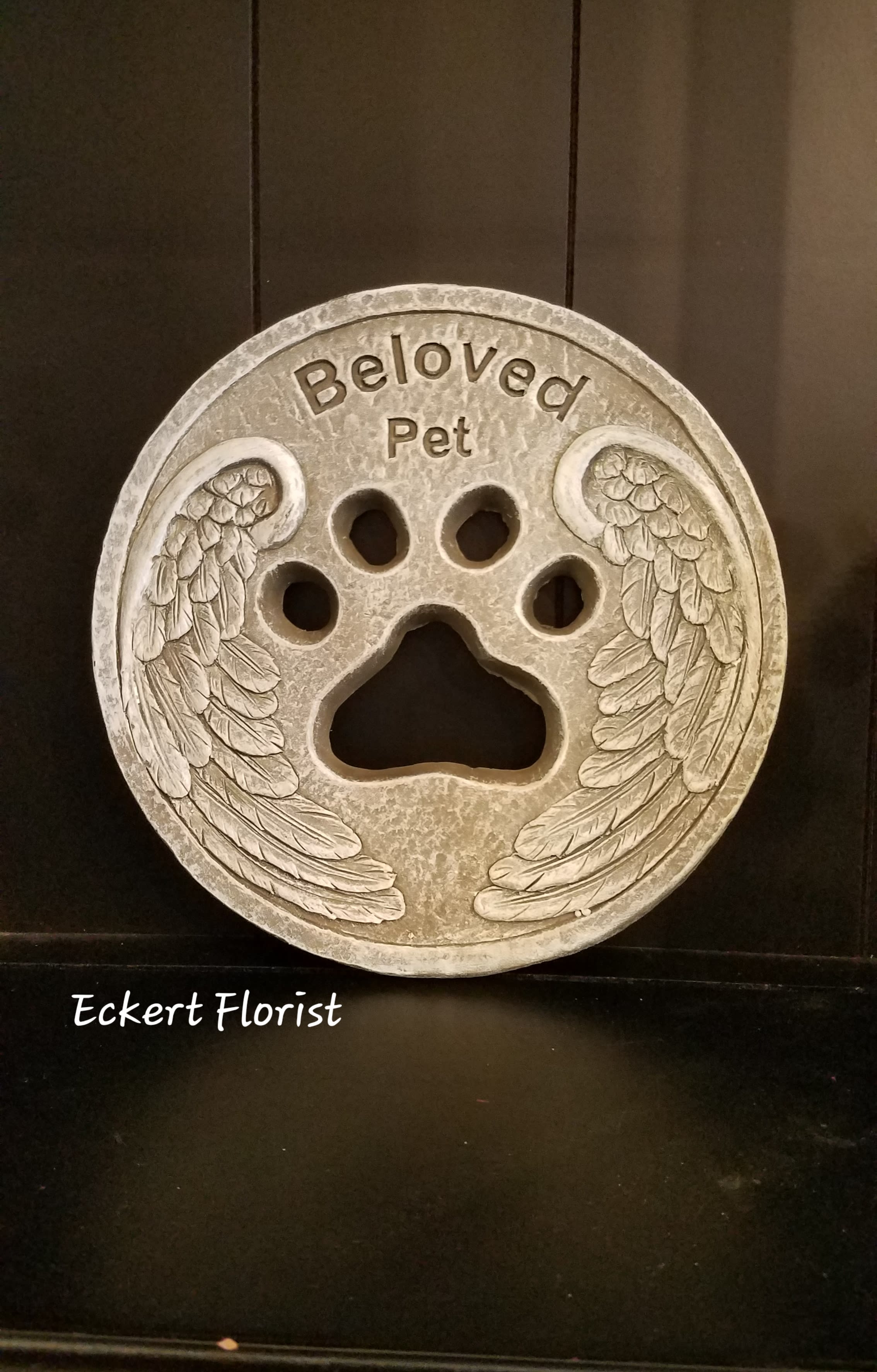 Round memorial plaque with a paw print and angel wings reading "Beloved Pet"