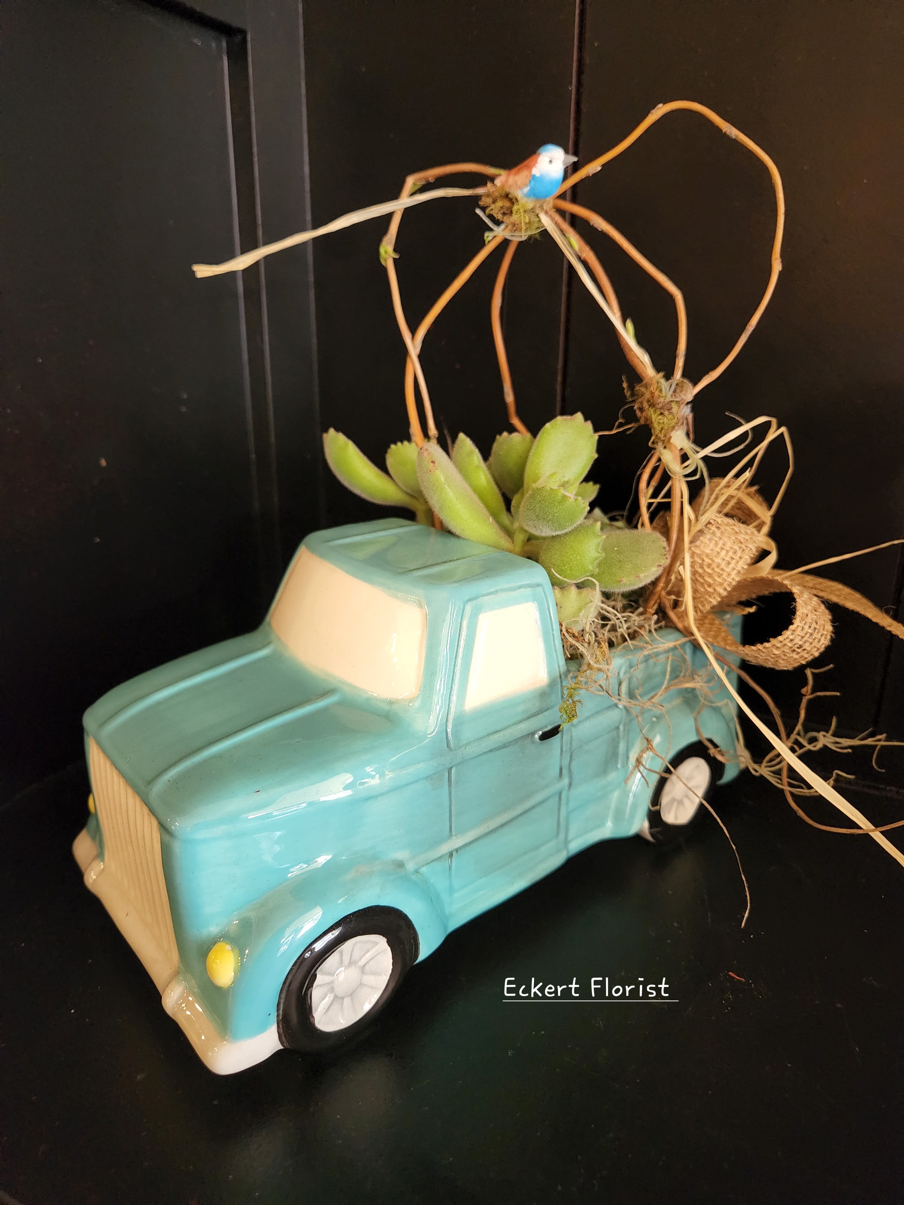 Succulent arrangement in a turquoise ceramic truck planter with a small bird topper