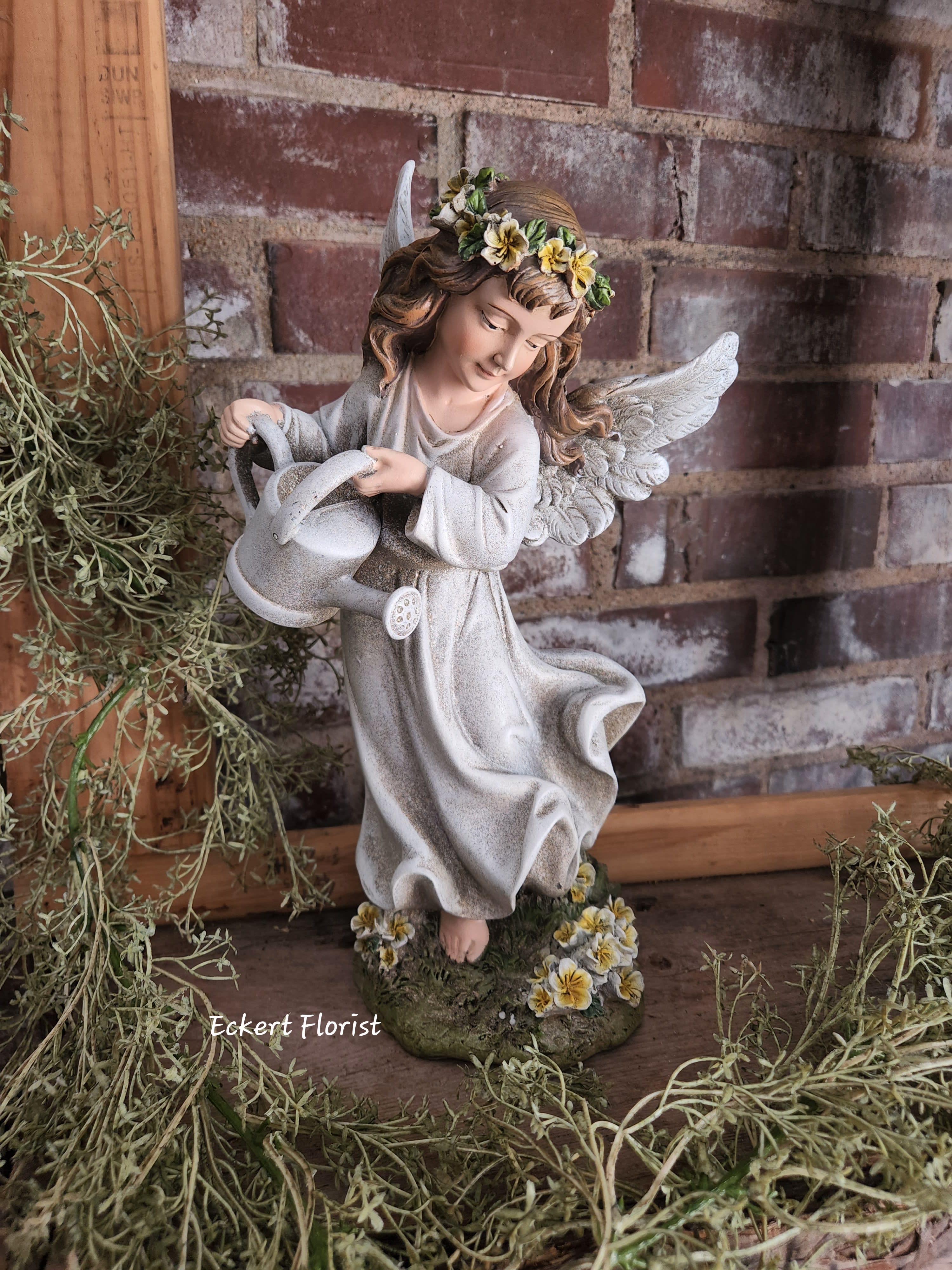 Angel figurine holding a watering can with small flowers on her head and base