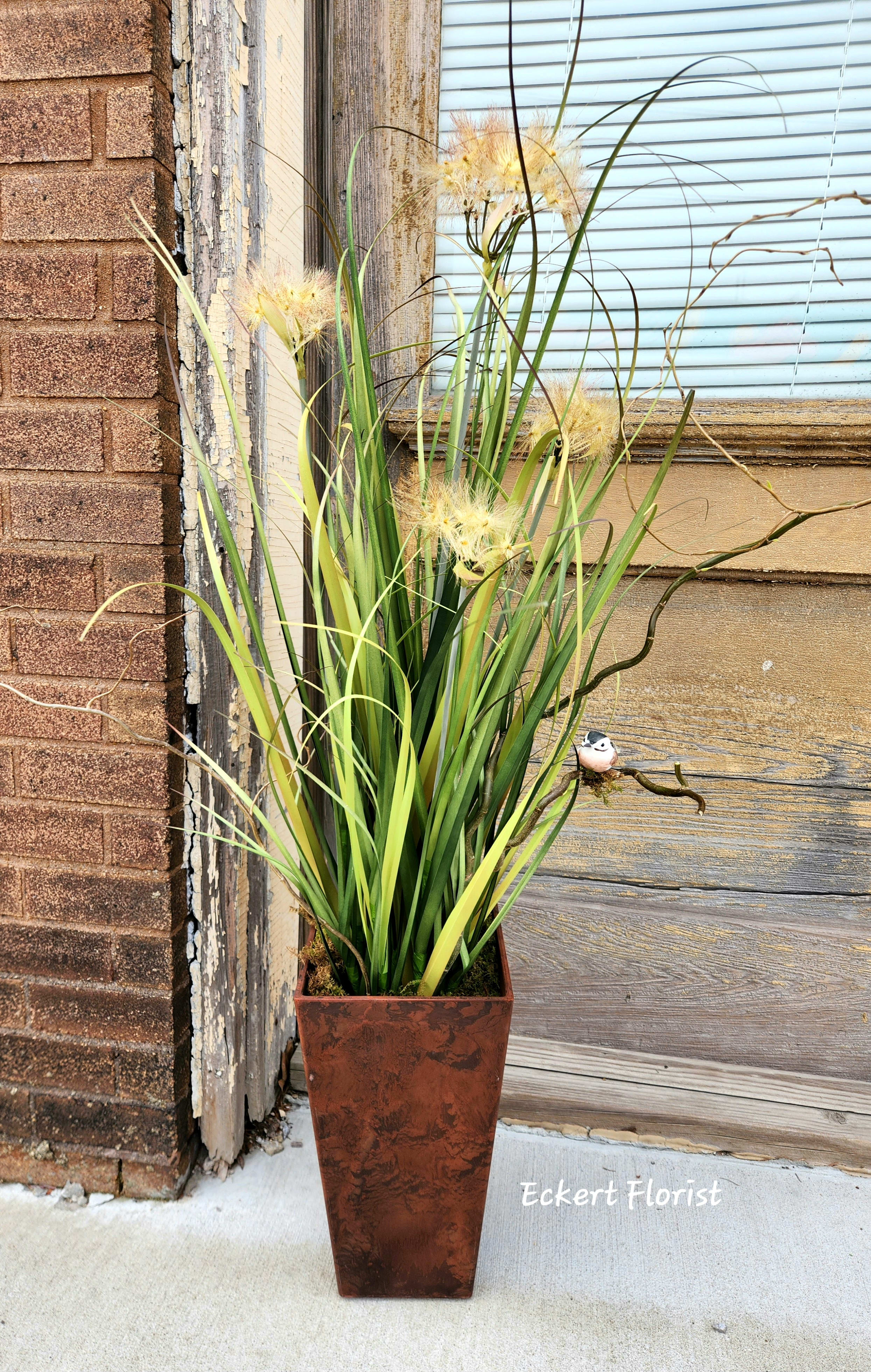 Tall potted arrangement with long grass-like leaves and pale yellow blooms
