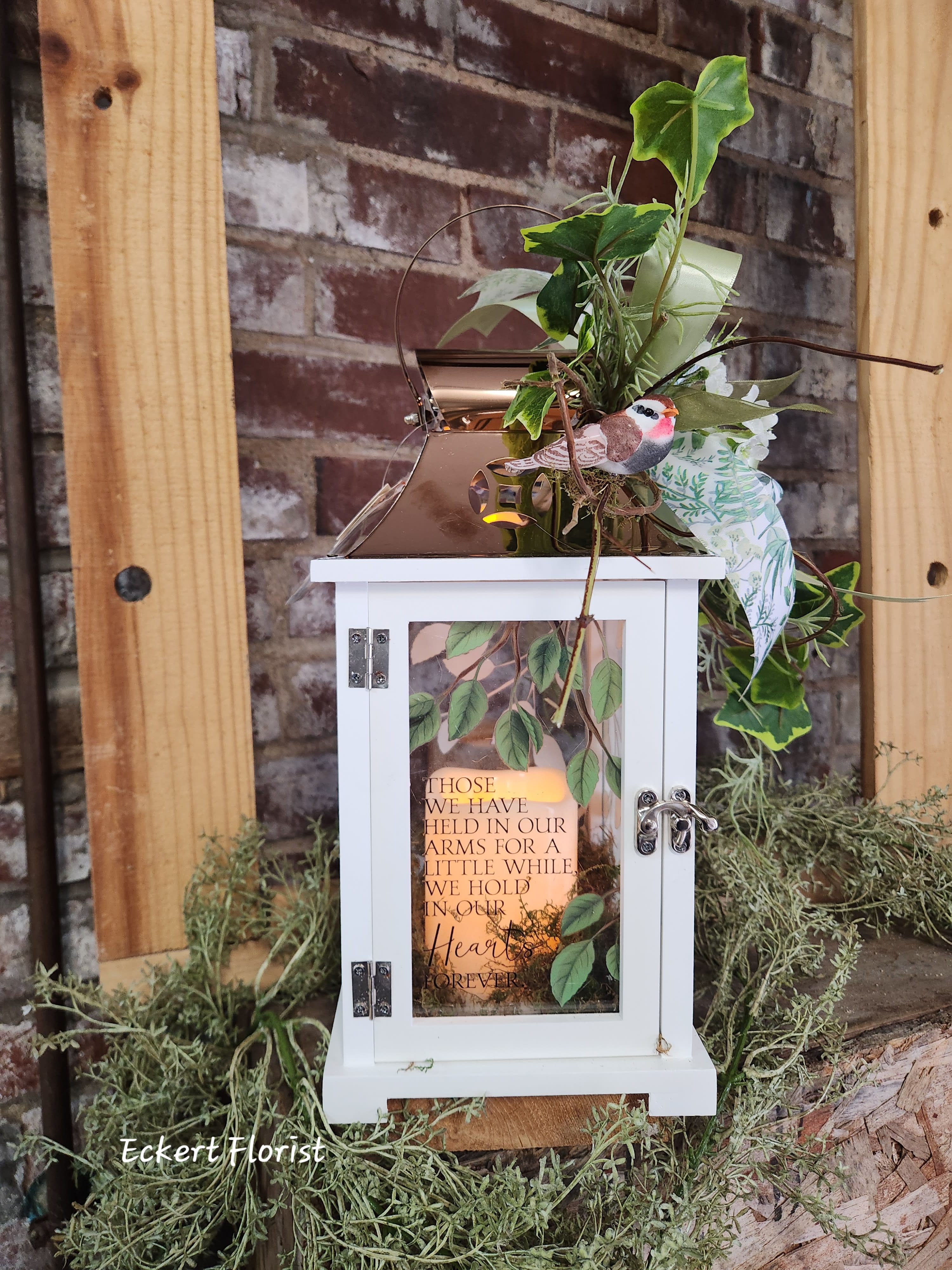 White lantern with greenery and a memorial message