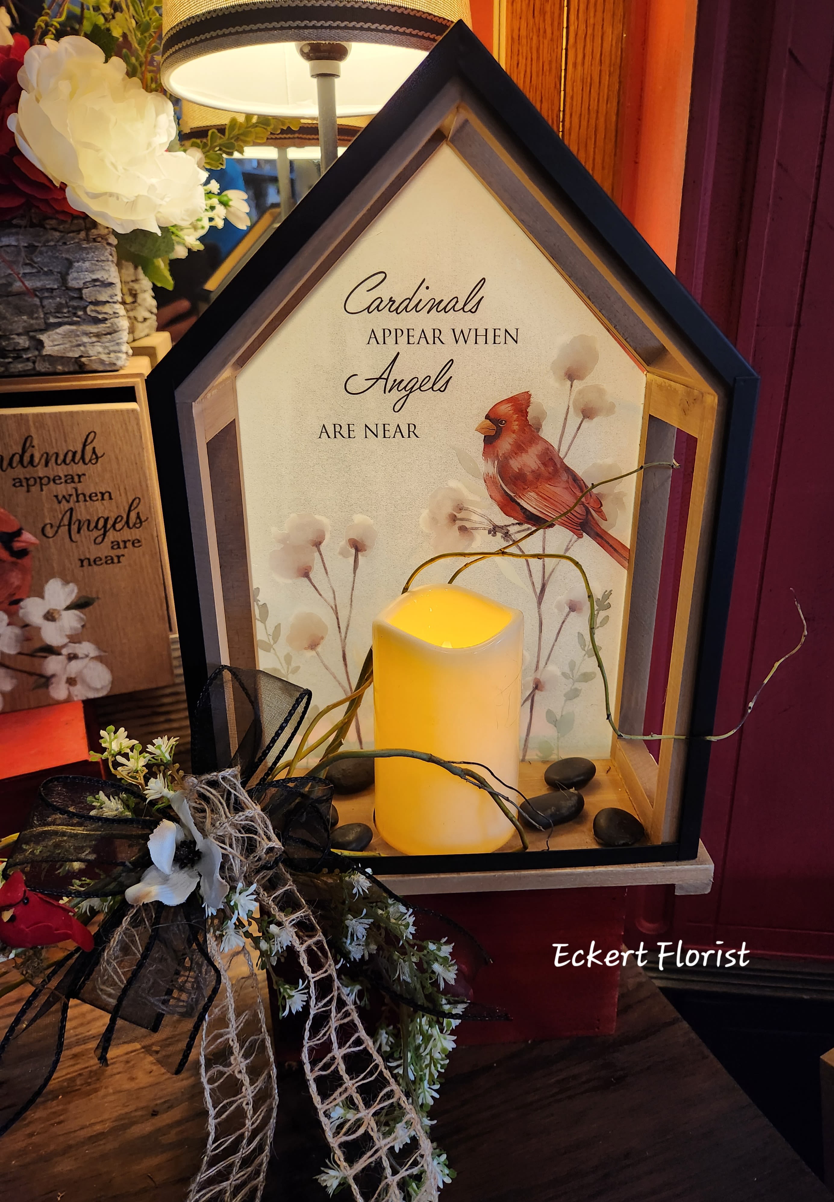 House-shaped memorial lantern with a lit candle and cardinal artwork
