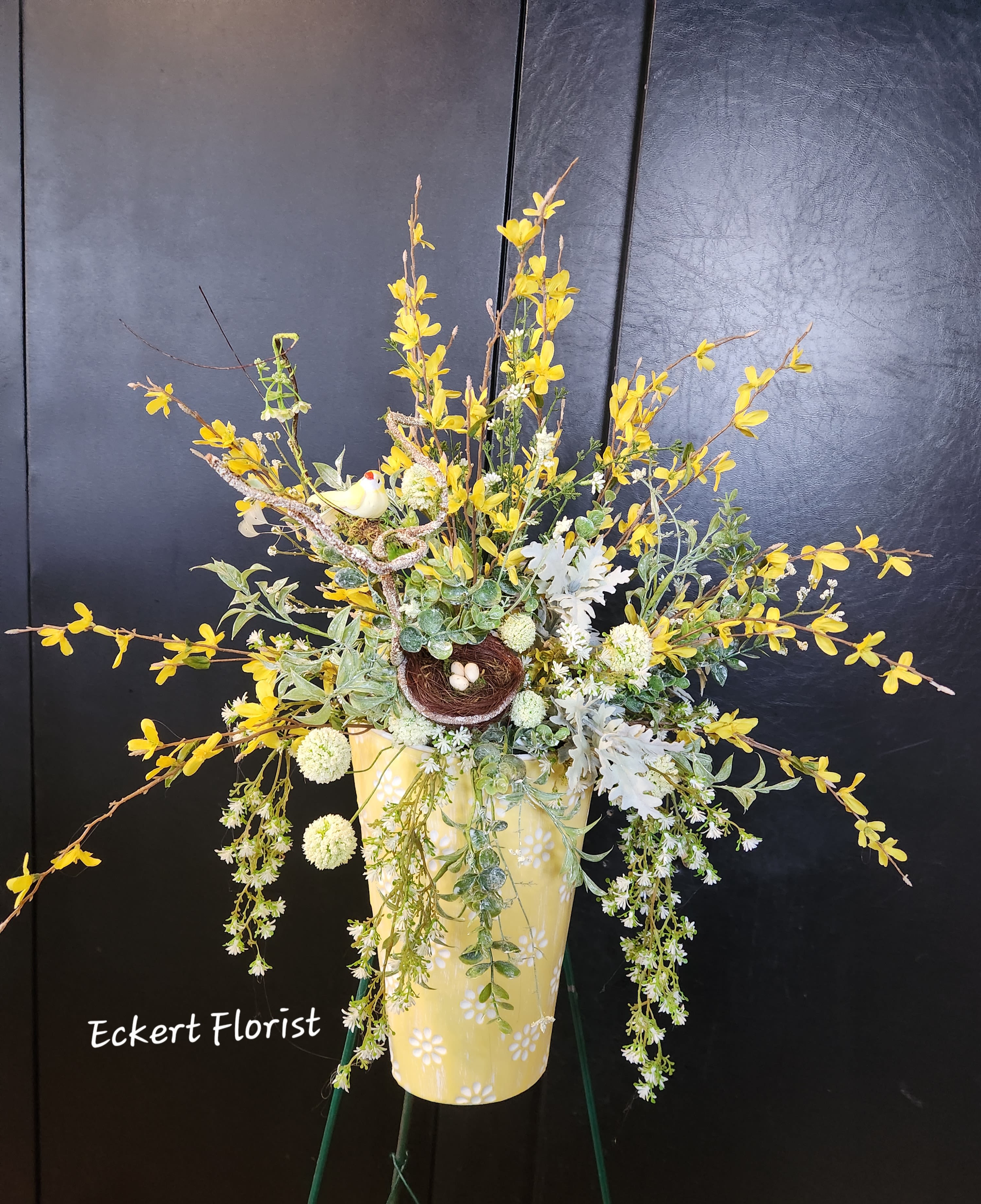 Yellow floral arrangement in a decorative vase with a small bird nest accent