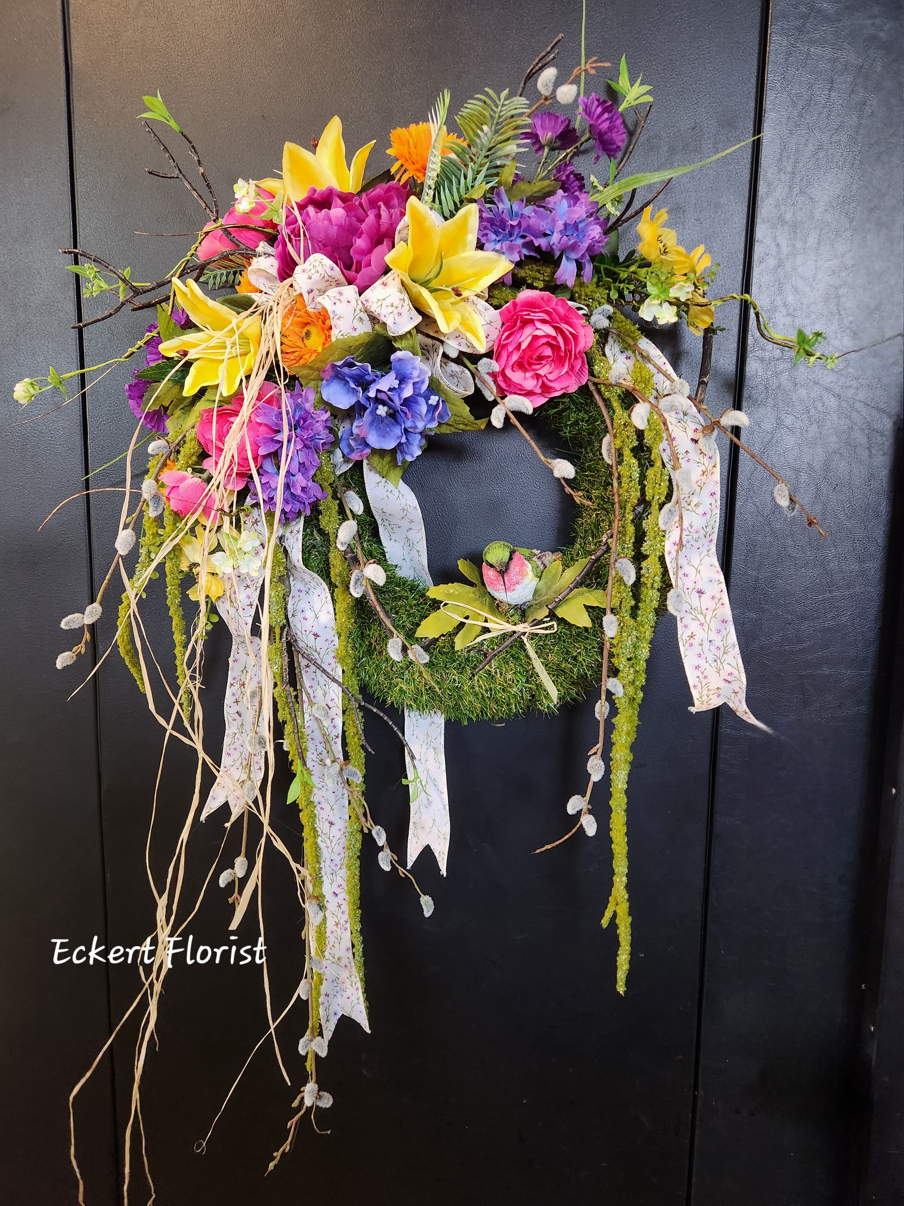 Colorful floral wreath with lilies, roses, and ribbons on a dark door
