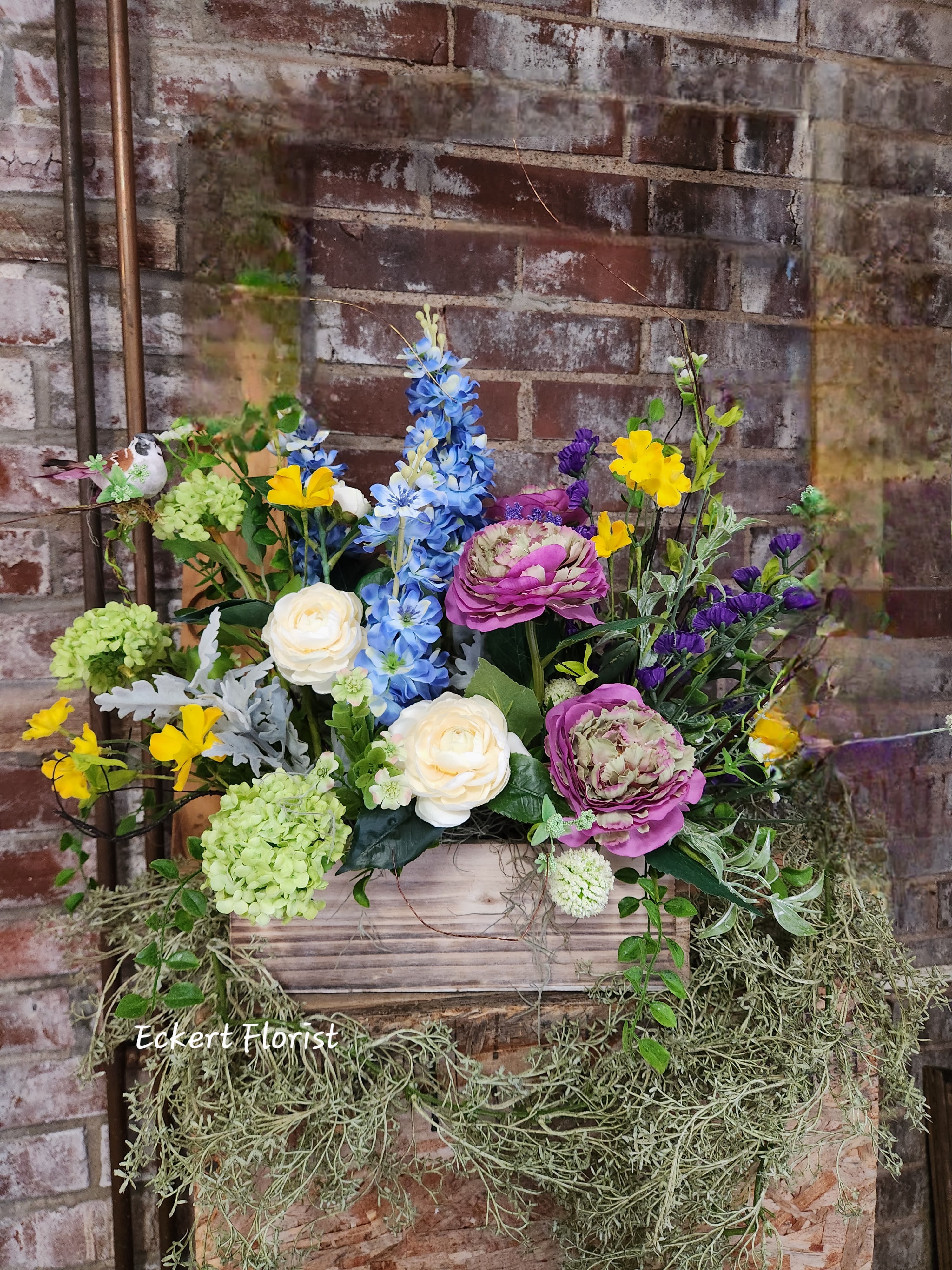 Mixed floral arrangement in a wooden box with blue, pink, yellow, and white blooms