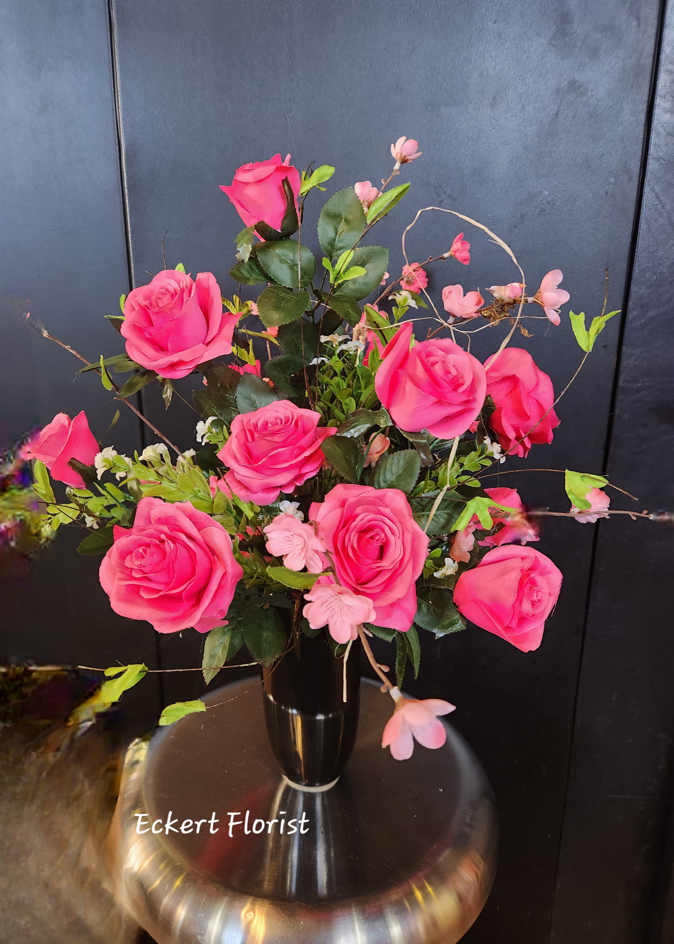 Pink roses arranged in a black vase with small pink blossoms