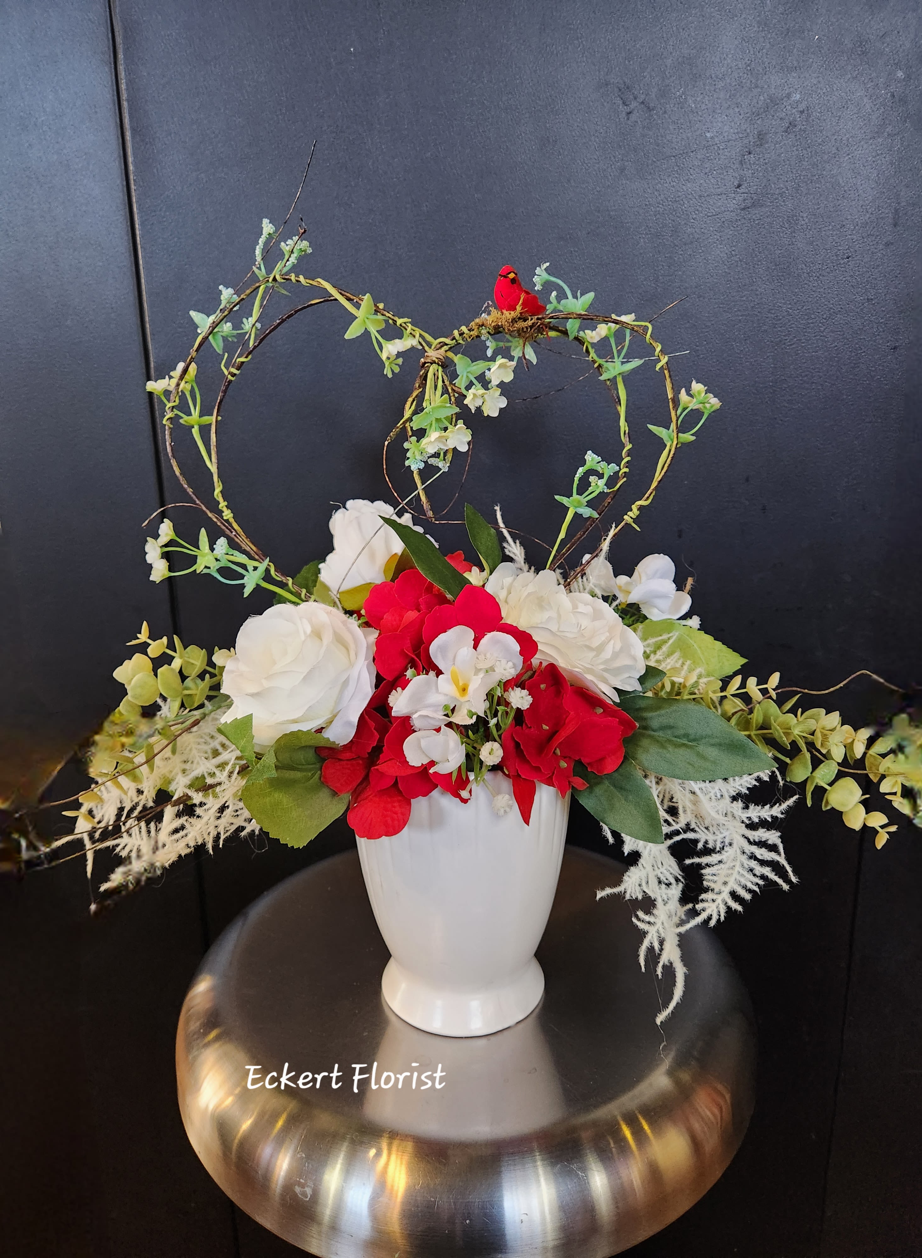 Red and white floral arrangement in a white vase with heart-shaped twig accents