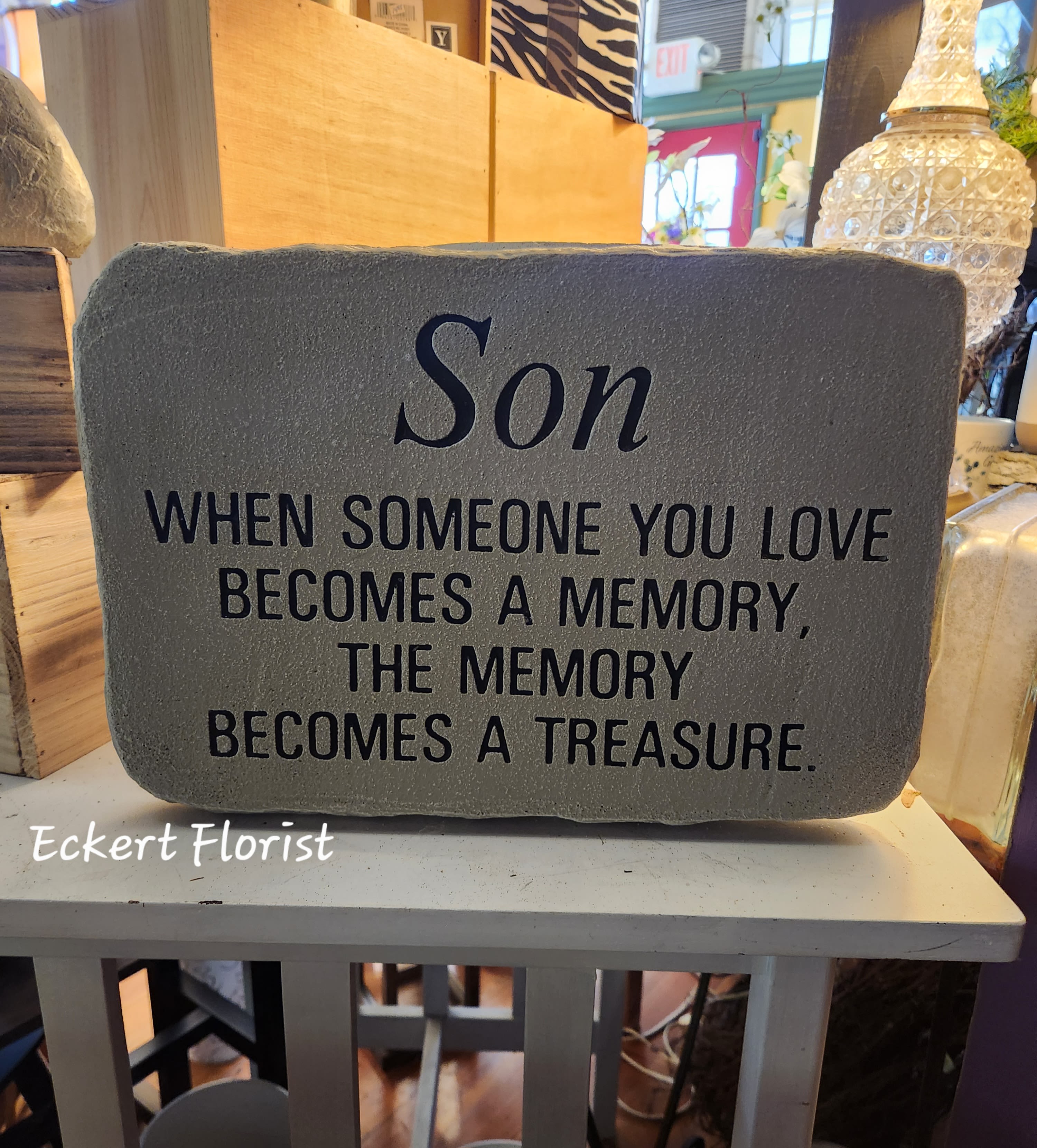 Eckert Florist's "Son..." Memorial Stone - "Son, When someone you love becomes a memory, the memory becomes a treasure." Cement Stone measures approx. 10" H X 14.5" W *Upgrade with artificial flowers. See Deluxe option. ALL OF OUR STONES COME DECORATED WITH A SHEER BOW, WILLOW, RAFFIA, AND OUR SIGNATURE BIRD.