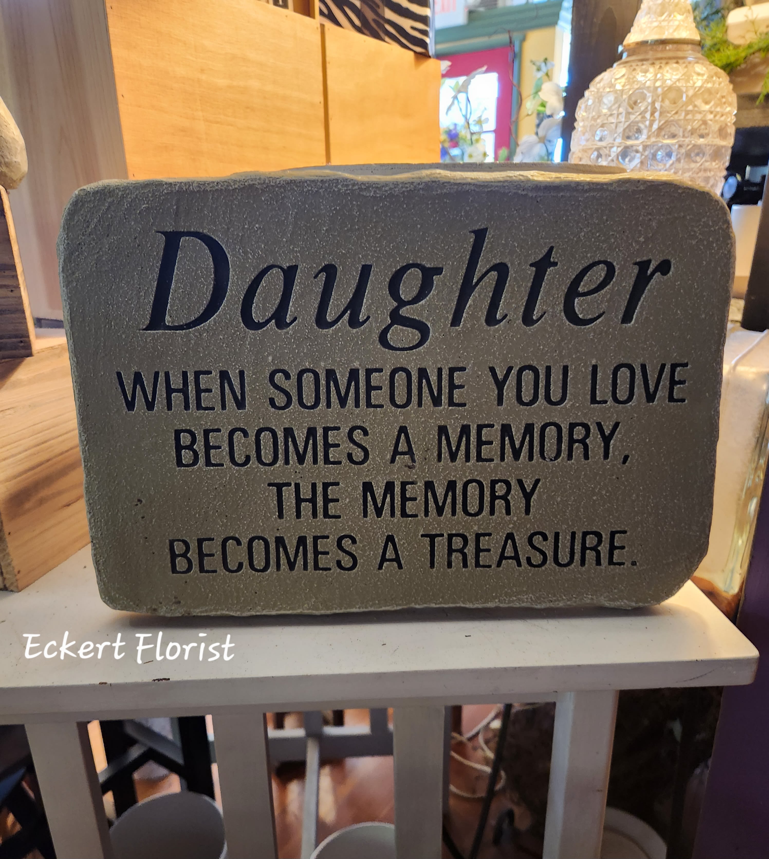 Eckert Florist's "Daughter.." Memorial Stone - "Daughter, When someone you love becomes a memory, the memory becomes a treasure." Cement Stone measures approx. 10" H X 14.5" W *Upgrade with artificial flowers. See Deluxe option. ALL OF OUR STONES COME DECORATED WITH A SHEER BOW, WILLOW, RAFFIA, AND OUR SIGNATURE BIRD.