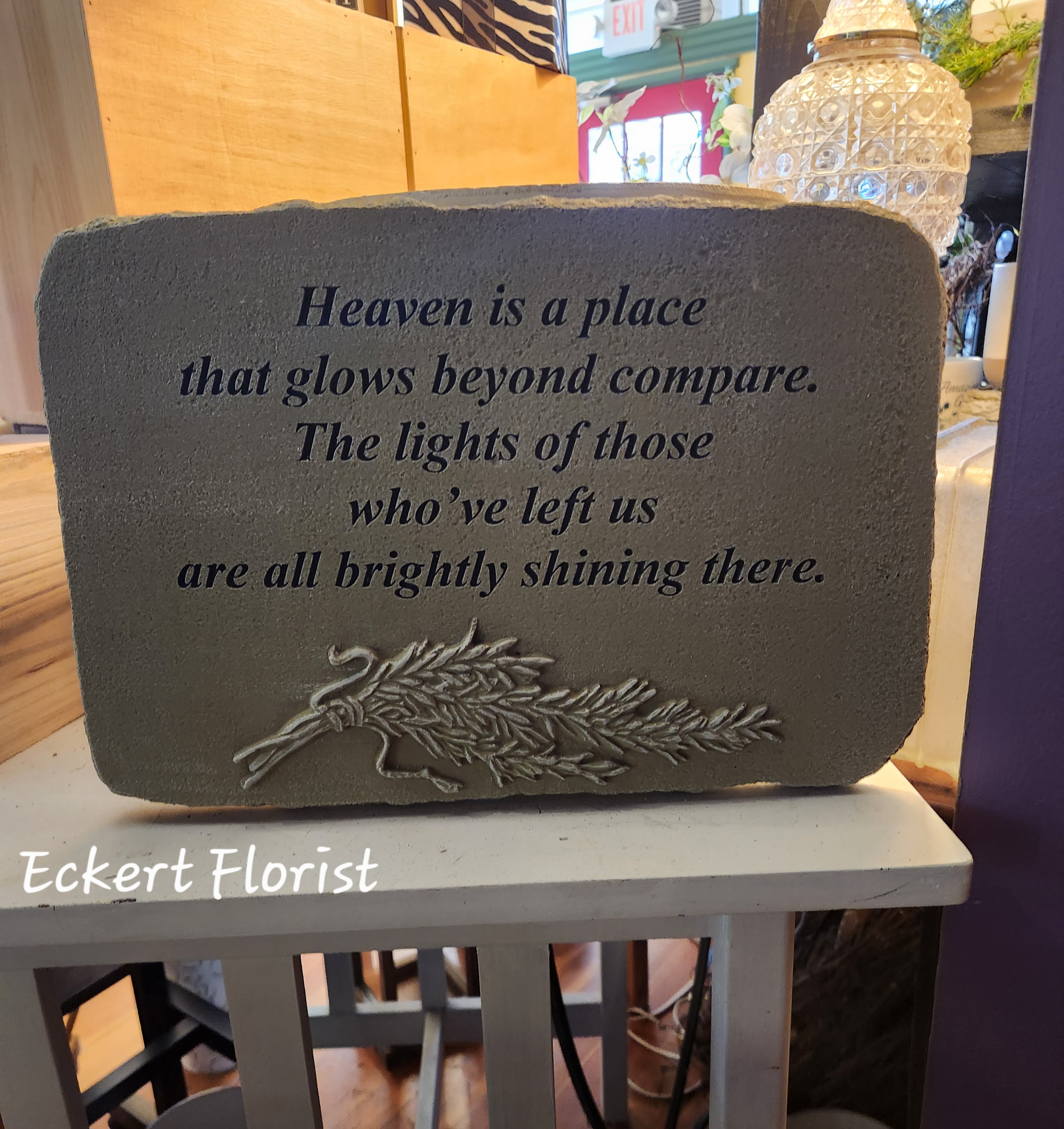 Eckert Florist's "Heaven is a place..." Memorial Stone - "Heaven is a place that glows beyond compare. The lights of those who've left us are all brightly shining there." Cement Stone measures approx. 10" H X 14.5" W *Upgrade with artificial flowers. See Deluxe option. ALL OF OUR STONES COME DECORATED WITH A SHEER BOW, WILLOW, RAFFIA, AND OUR SIGNATURE BIRD.