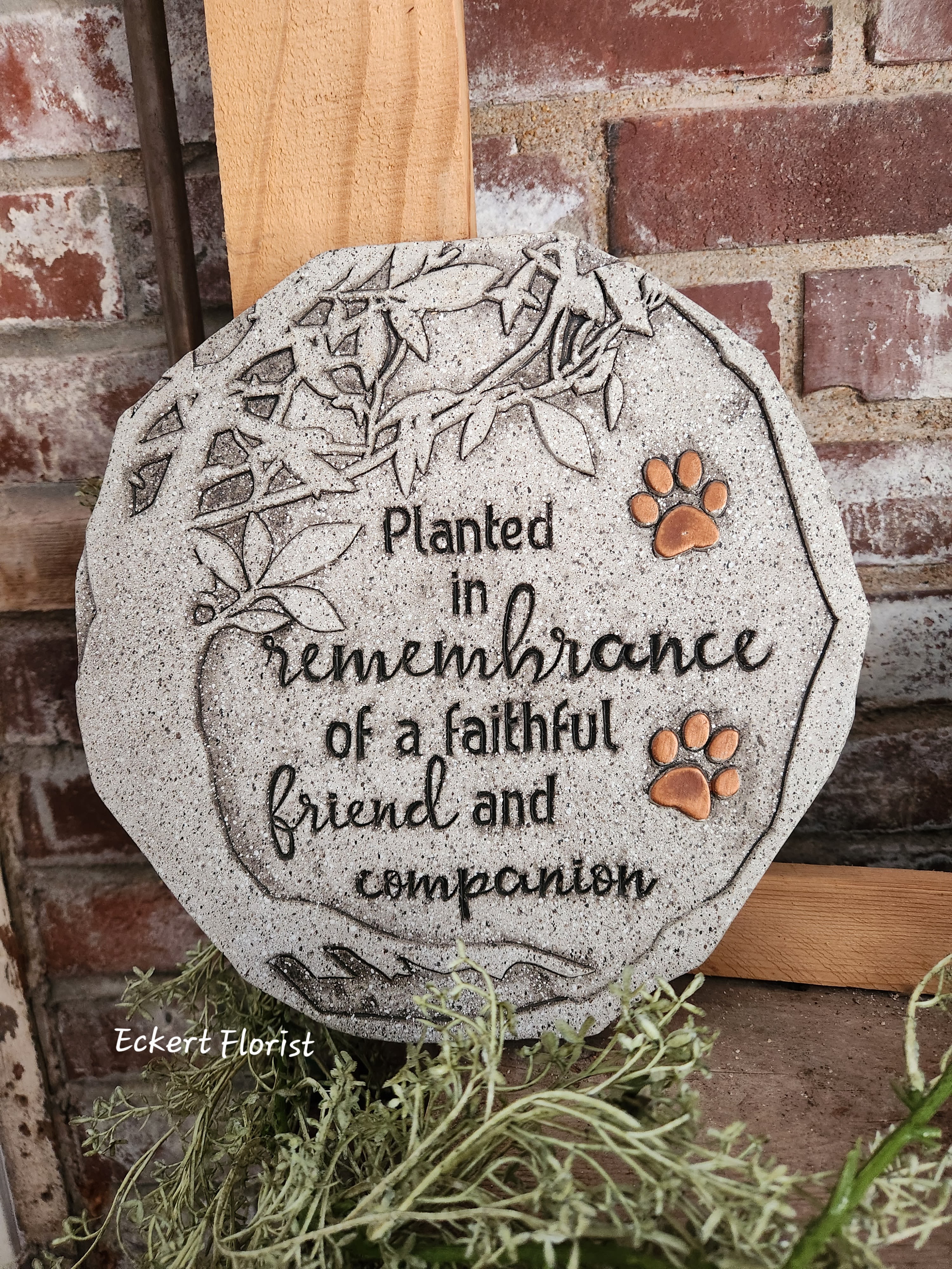 Eckert Florist's "Planted In Remembrance..." Pet Memorial Stone - This Garden Stone is hand painted and cast in resin to emulate the look of stone and antiqued bronze. Includes a keyhole hanger for easy hanging. *May be added to a fresh arrangement or green plant. See Deluxe and/or Premium upgrades. *See Add-on Section for Display Easel Approx.: D: 0.5" DIA: 10"