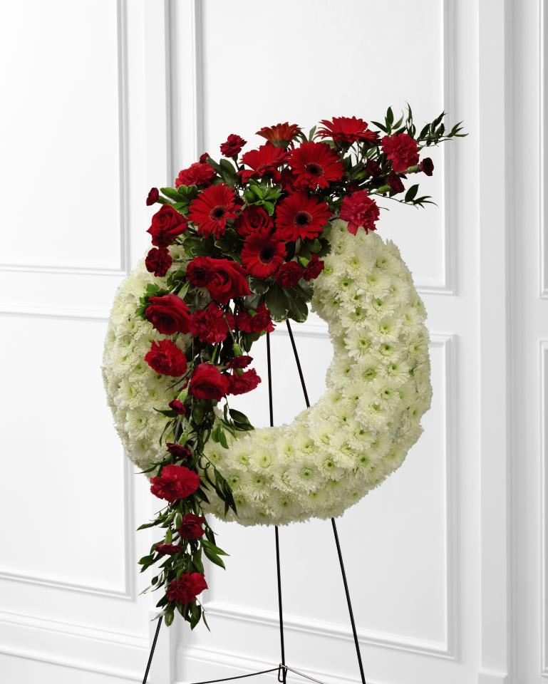FTD Graceful Tribute Wreath - The FTD Graceful Tribute Wreath creates a stunning presentation of love's serenity for their final farewell service. Red roses, carnations and gerbera daisies are accented with burgundy mini carnations and a variety of lush greens to create a sweeping arrangement  that glides across the face of a snow white wreath consisting of chrysanthemums making  this a remembrance for one who has touched your life like  none other. Displayed on a wire easel. 