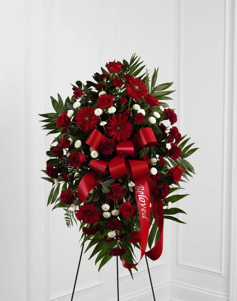 FTD Treasured Memories Standing Spray - "The FTD Treasured Memories Standing Spray is a rich and colorful way to express your unending love and devotion to the departed. An exceptional arrangement of red roses, burgundy carnations, burgundy mini carnations, red gerbera daisies and white button poms are accented with a variety of lush greens. A red ribbon with the word, ""Beloved,"" embossed in a gold metallic lettering, finishes this beautiful display for their final farewell service. Displayed on a wire easel.