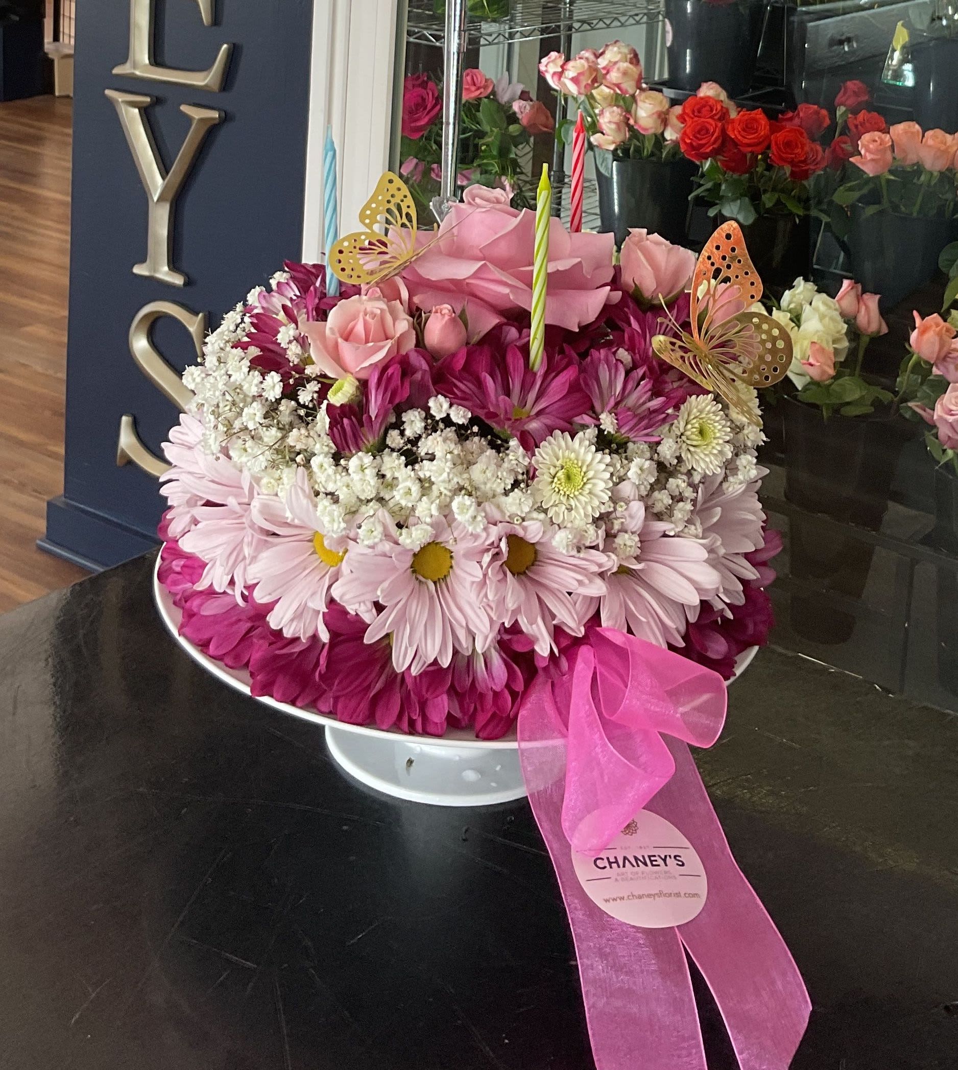 Pink floral arrangement with roses, daisies, and candles in a white pedestal bowl