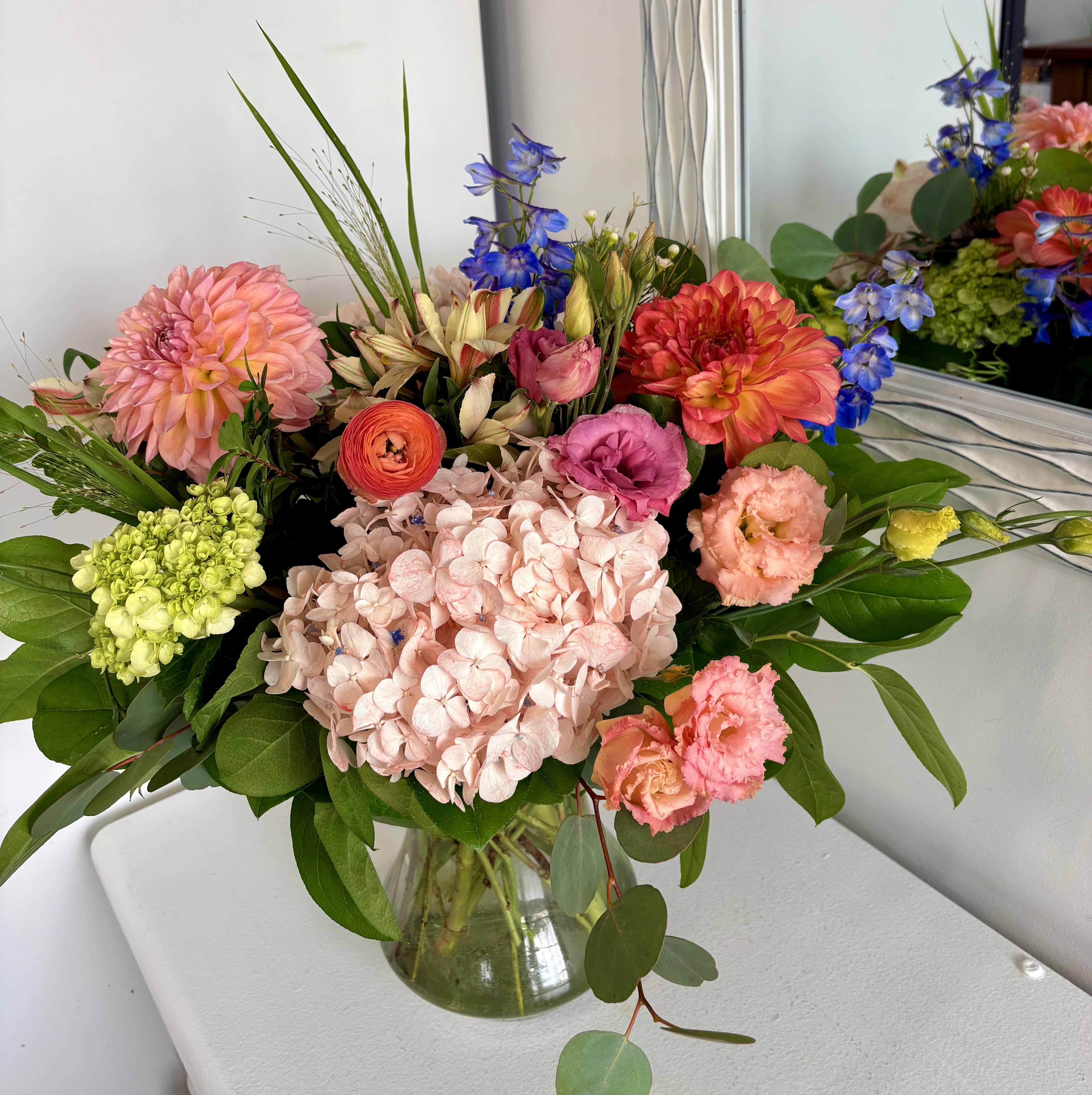 Mixed bouquet in a clear glass vase with pink, coral, blue, and green blooms