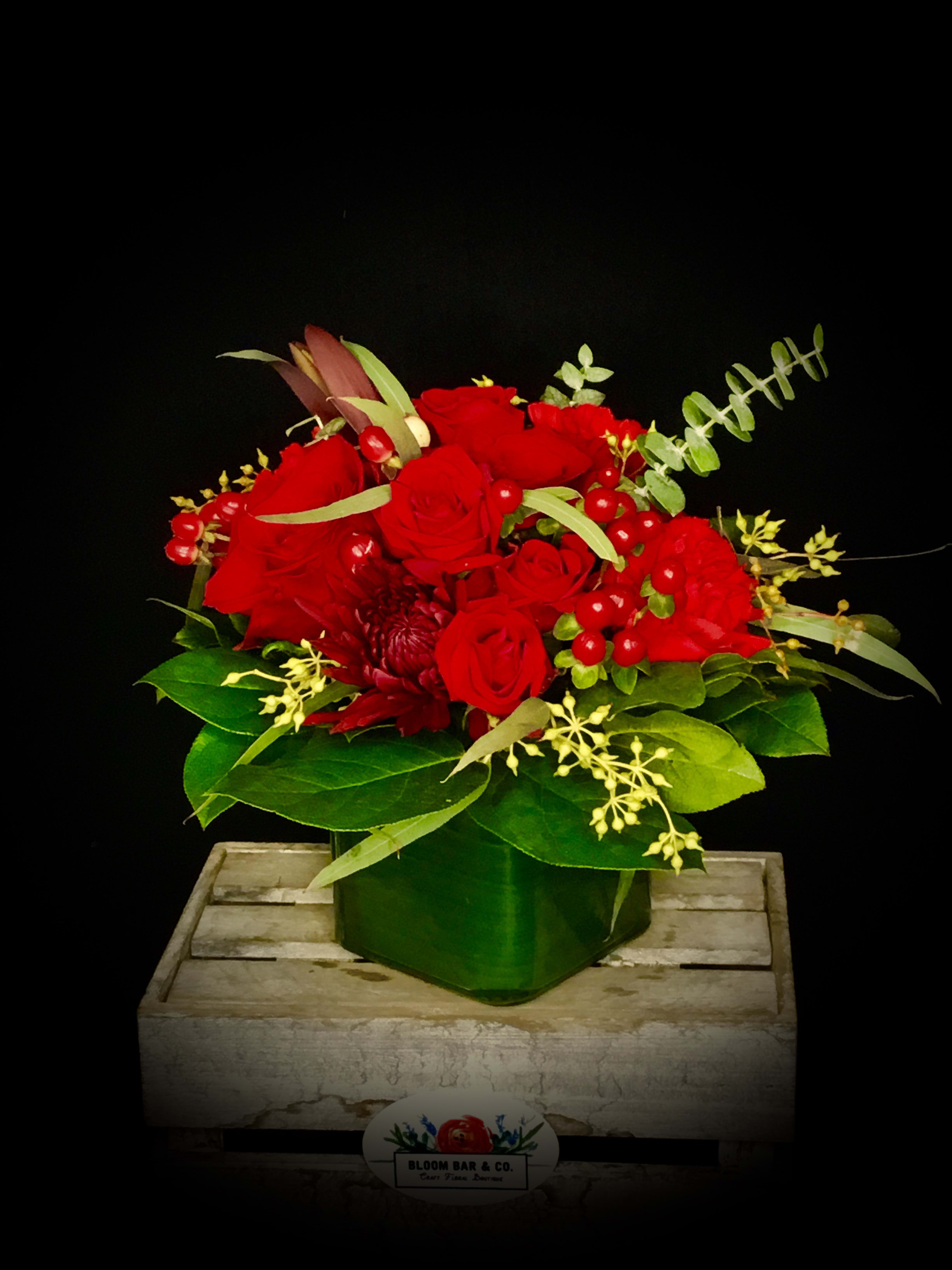 Red rose arrangement in a green vase with berries and greenery