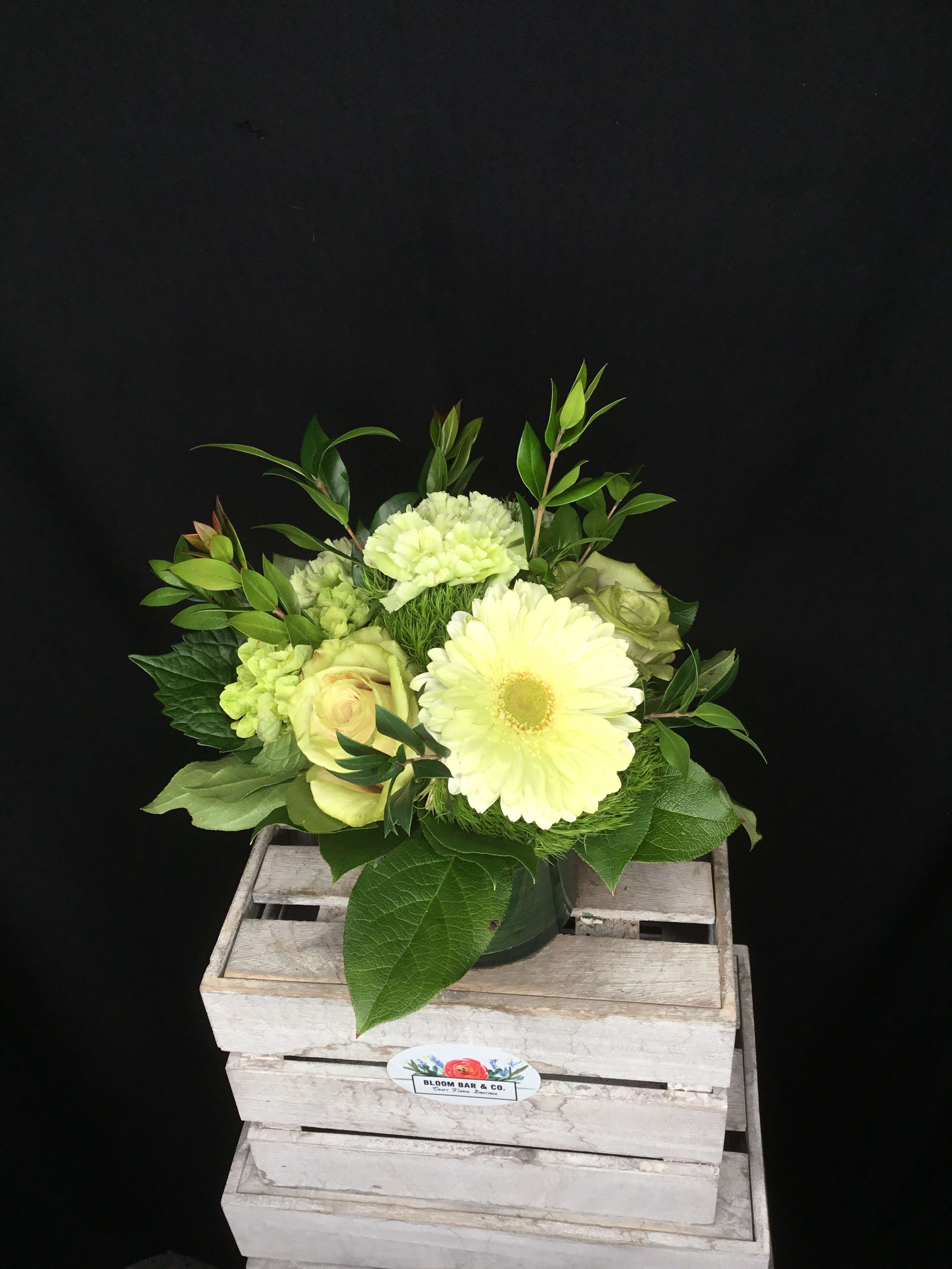 Pale yellow flower arrangement in a dark vase with greenery