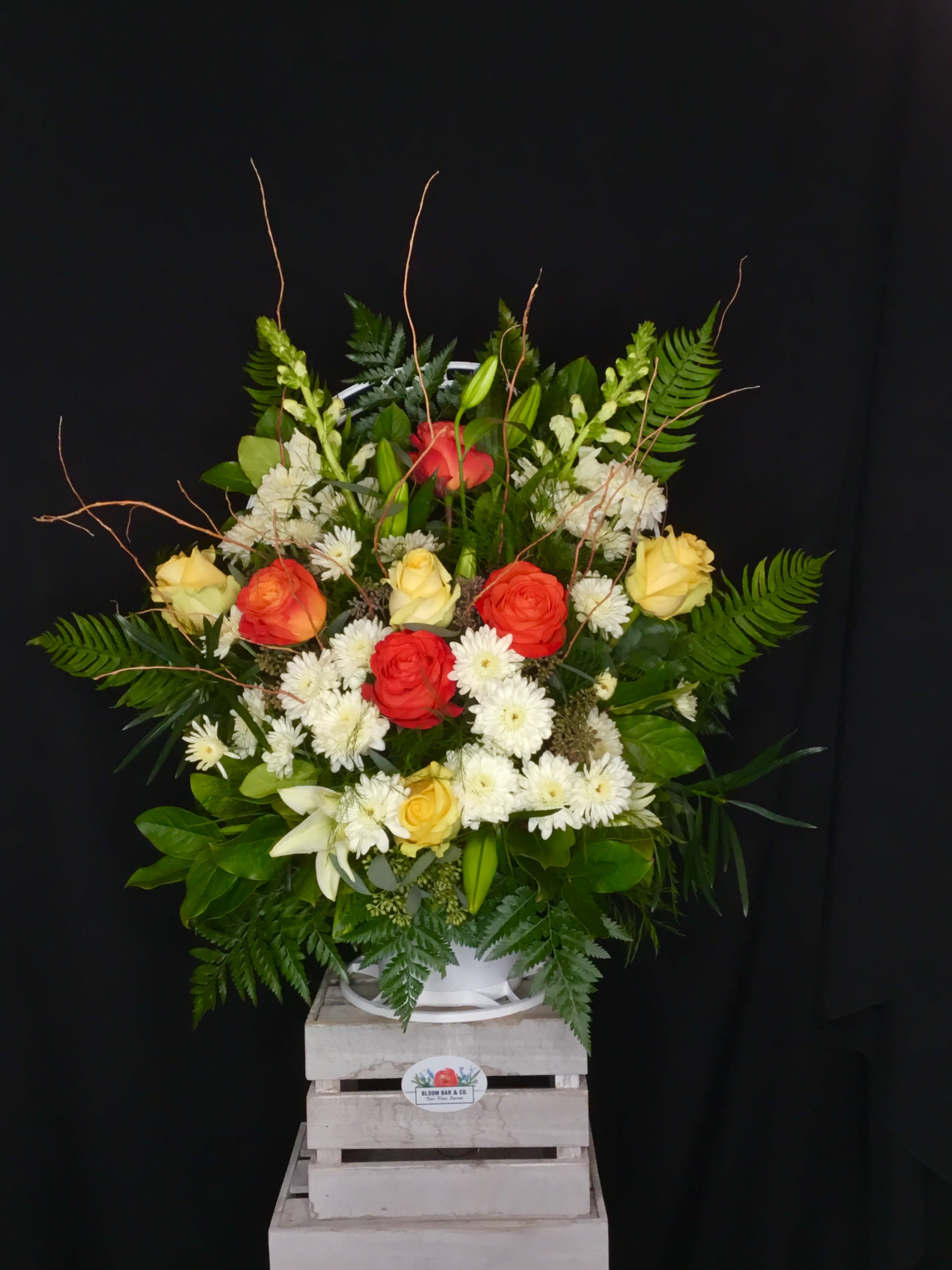 Large mixed bouquet of roses, lilies, and white daisies in a white container