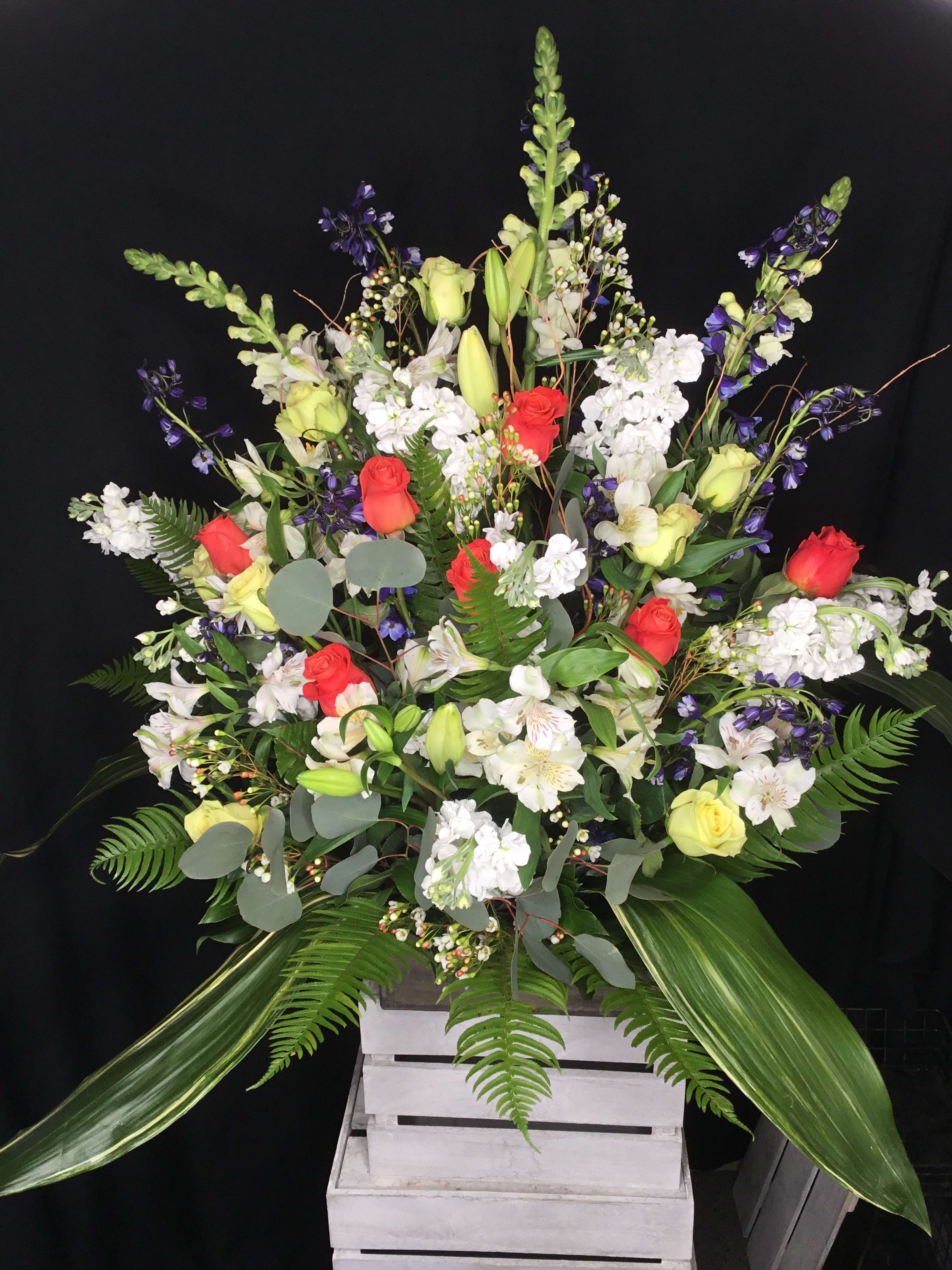 Large mixed floral arrangement with red and yellow roses in a white crate