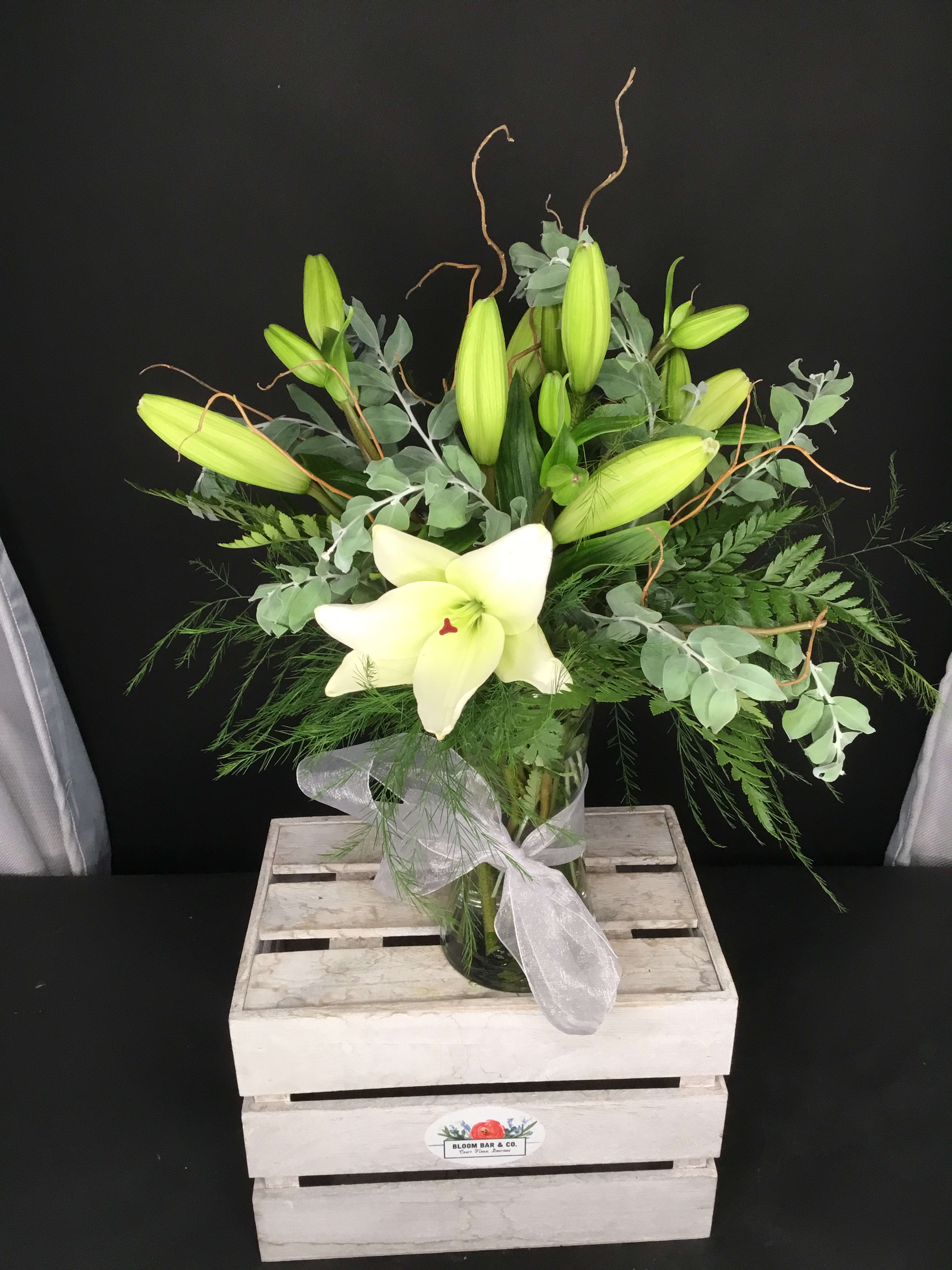 White lily arrangement in a glass vase with a sheer ribbon