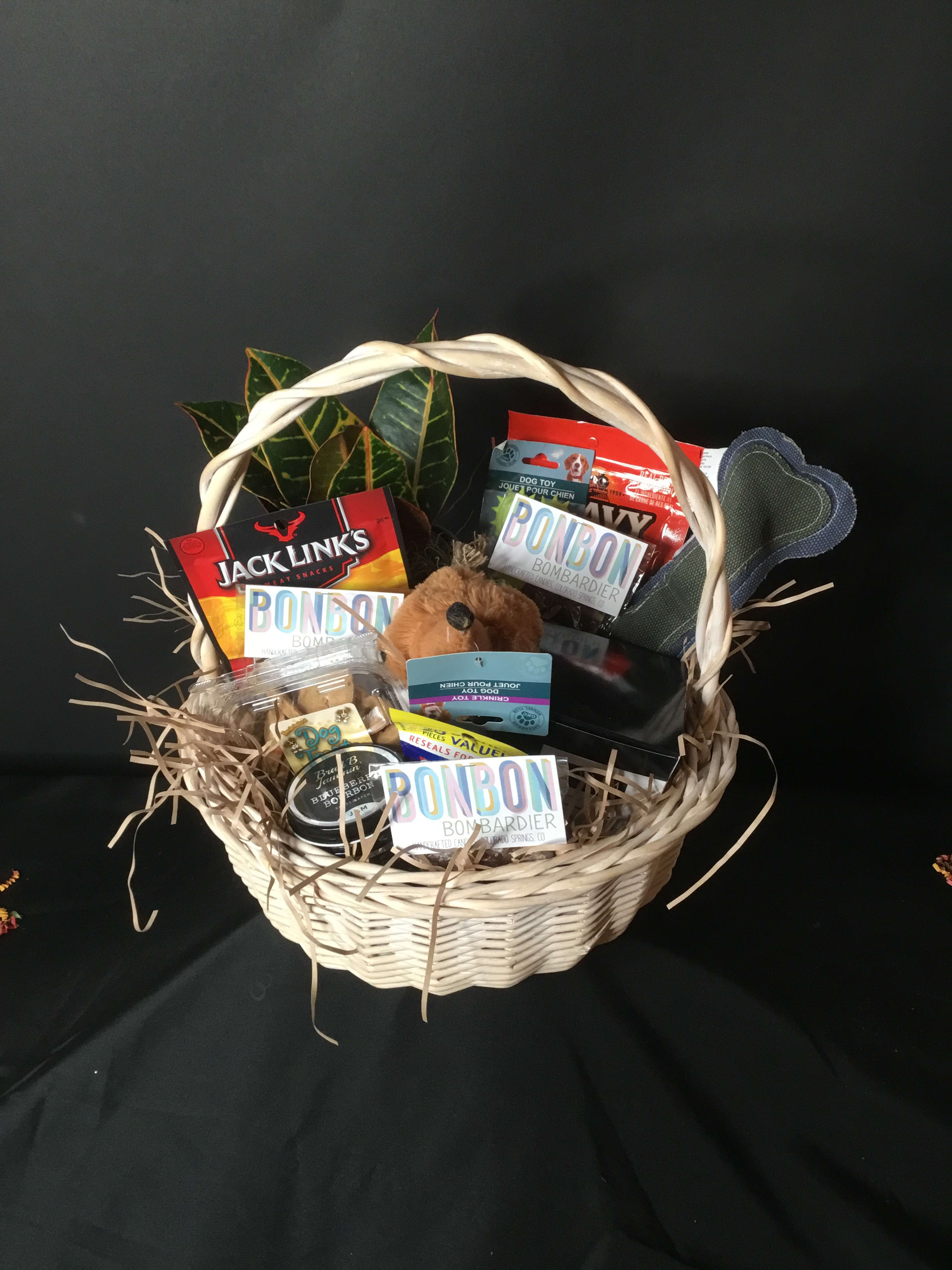 Gift basket with dog treats, toys, and a plush dog in a wicker basket